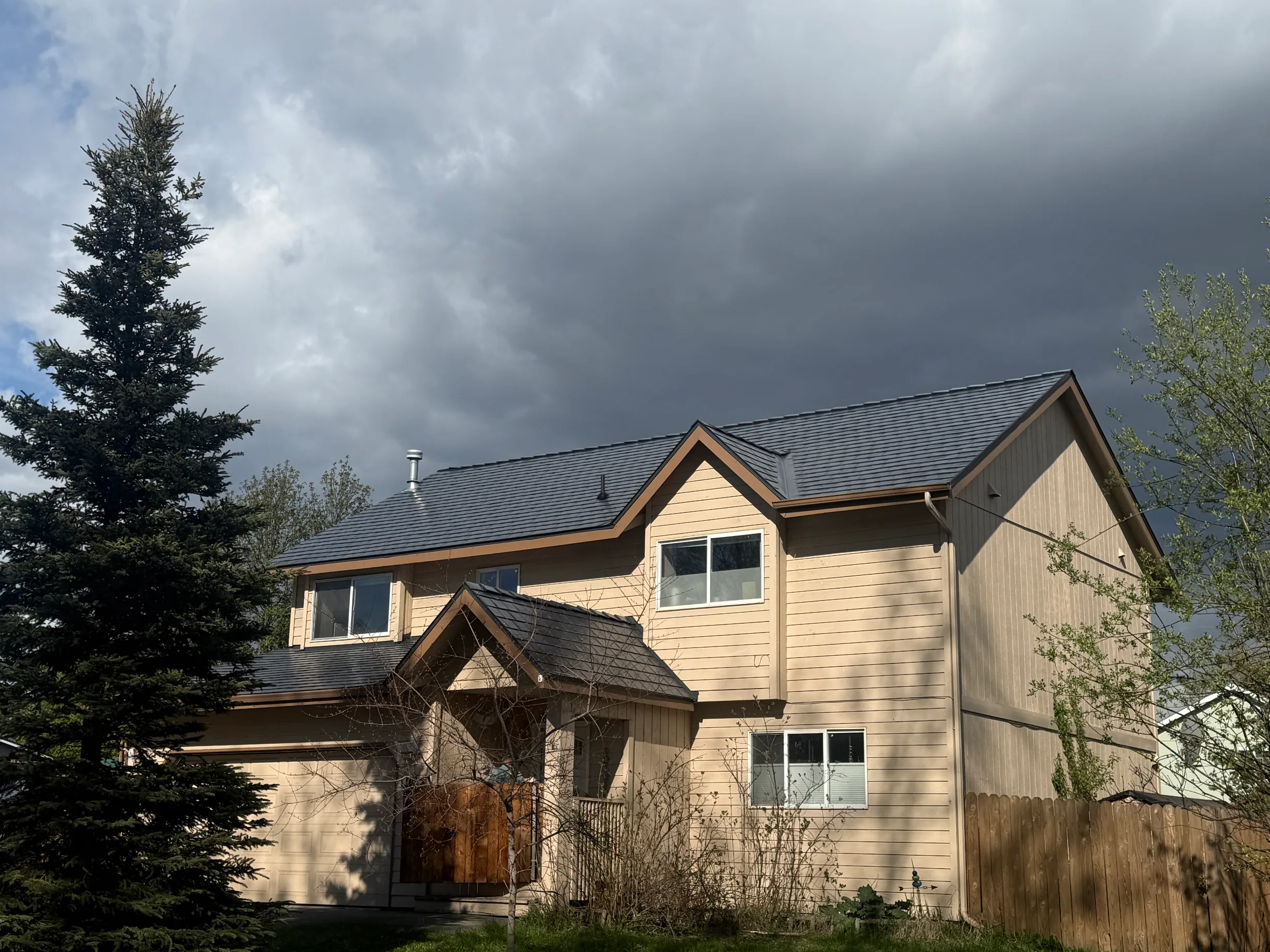 A modern-style home with a metal roof, tan siding and a brown door, under an overcast sky.