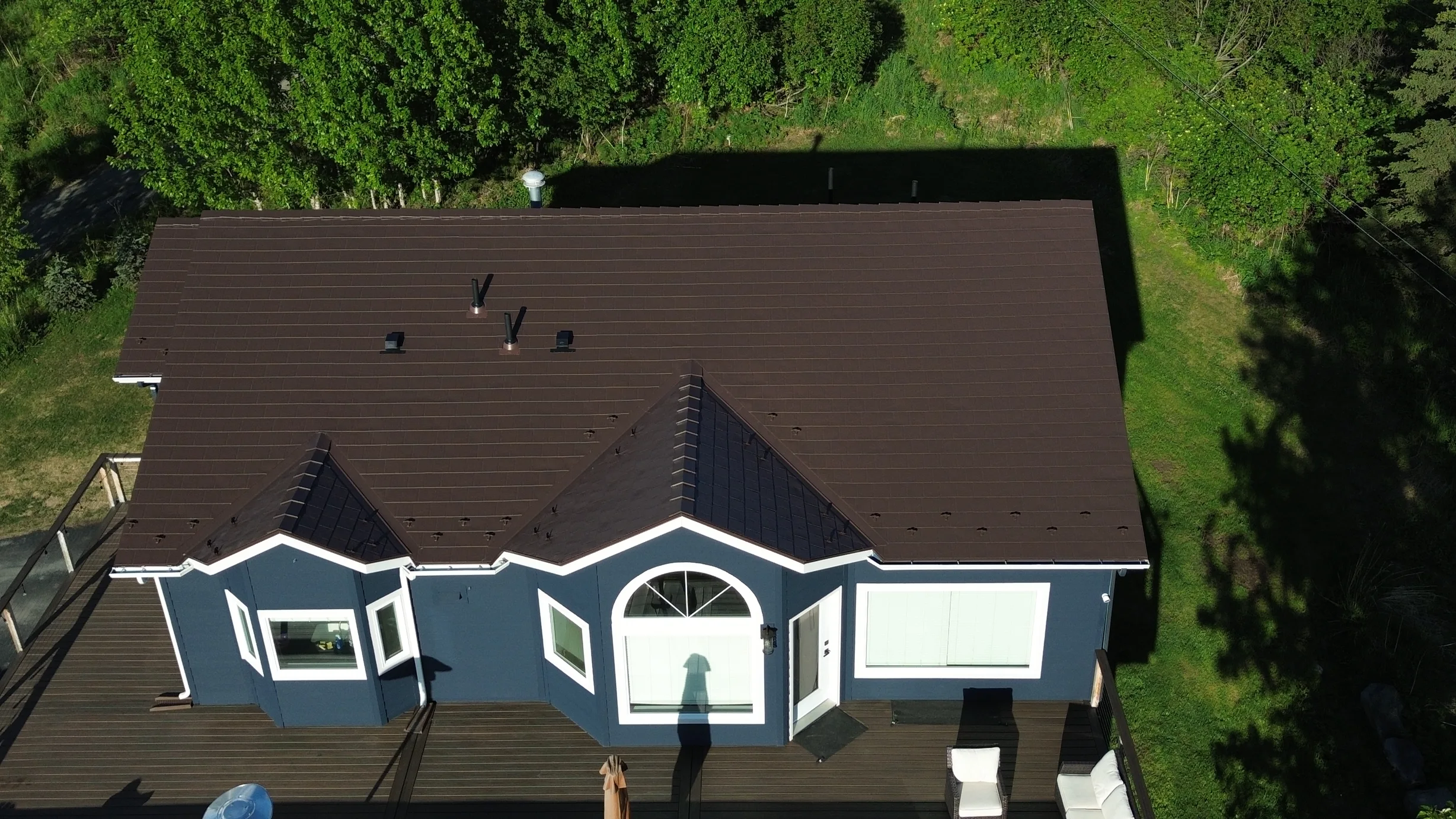 Aerial view of a finished brown metal roof on a single-family ranch-style home in a forested rural setting