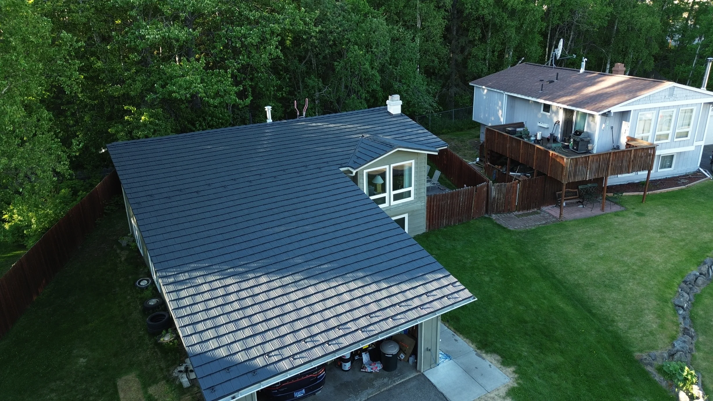 A blue metal roof on a white ranch-style home in a forested area