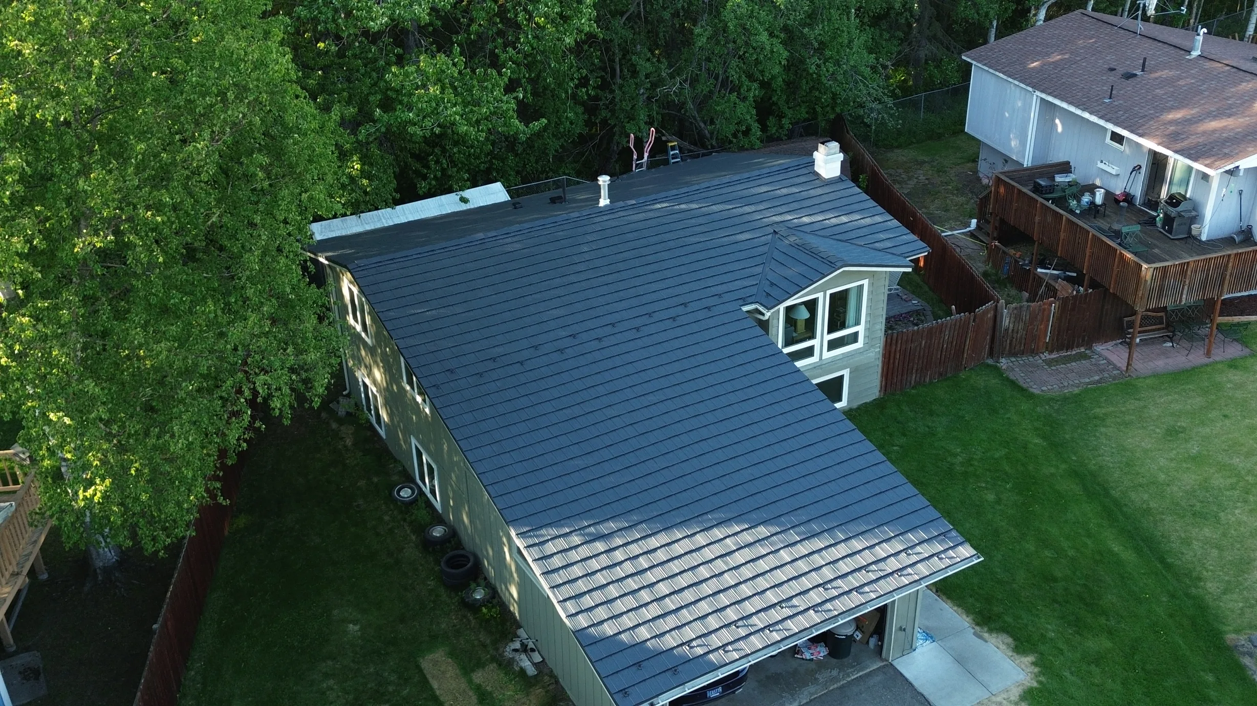 Aerial view of a finished metal roof on a ranch style home in a forested rural setting.