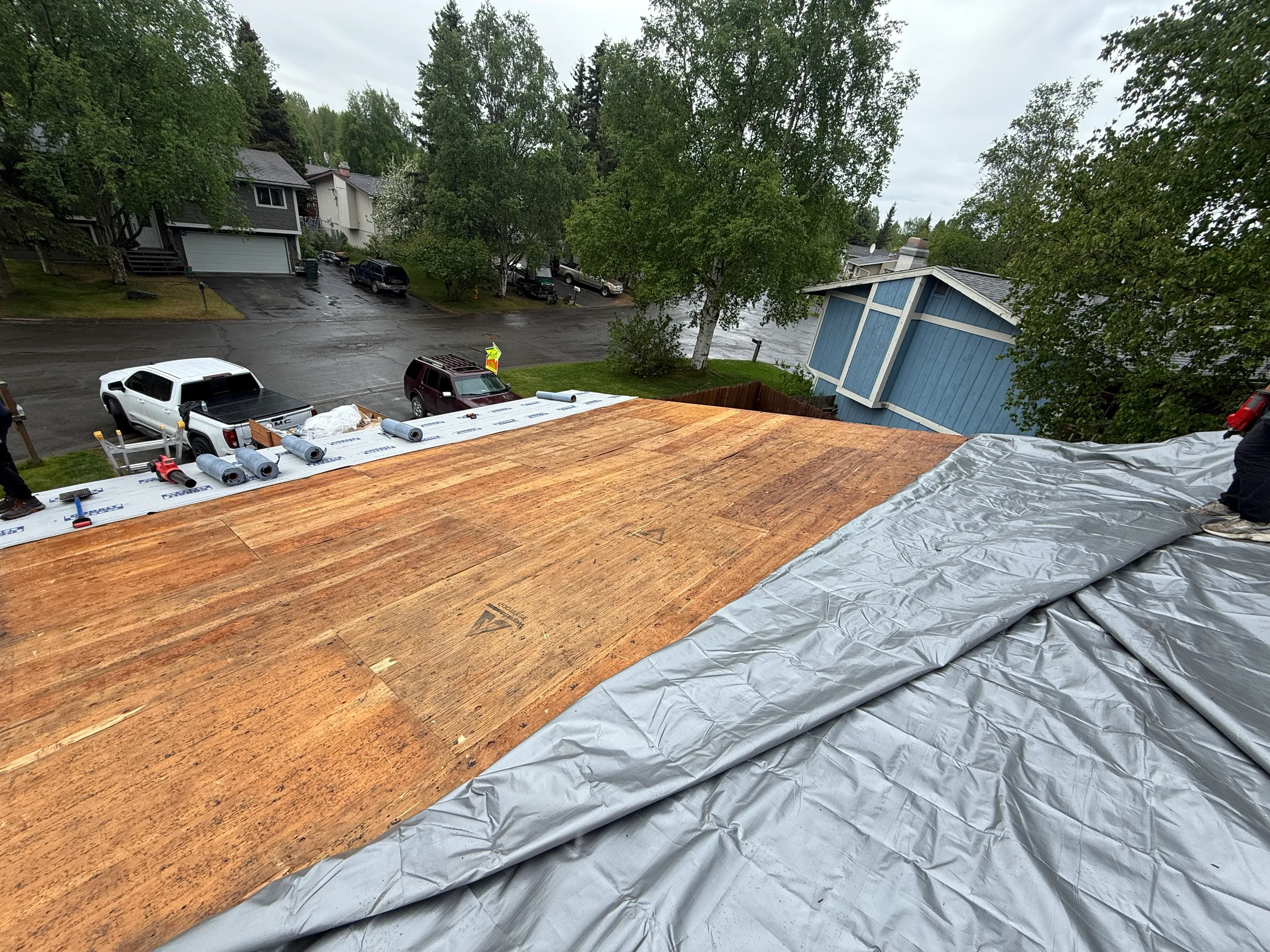 A metal roof under construction in a suburban area with lush greenery and an overcast sky.