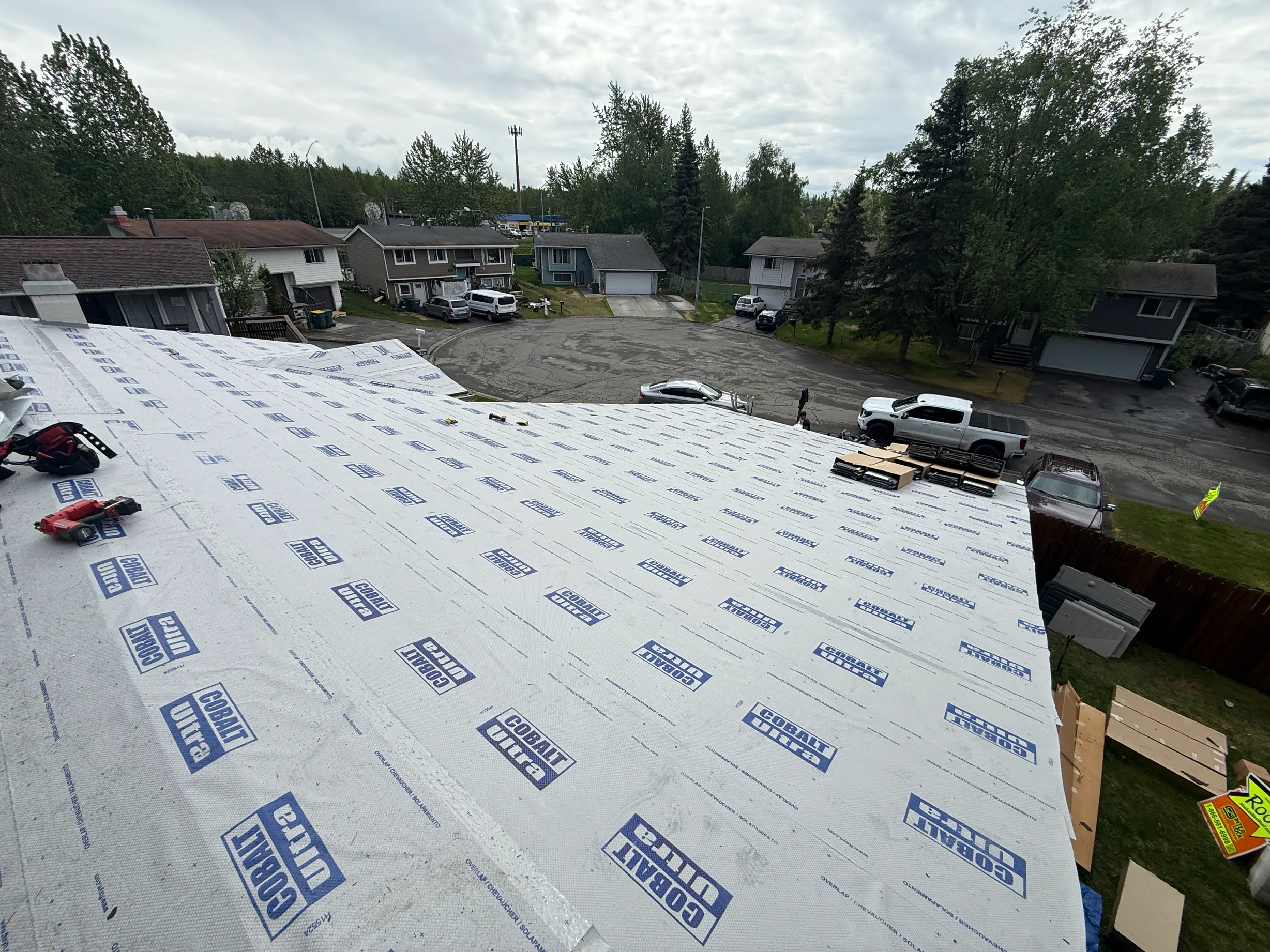 A modern metal roof is being installed on a single-family home in an urban forested setting.