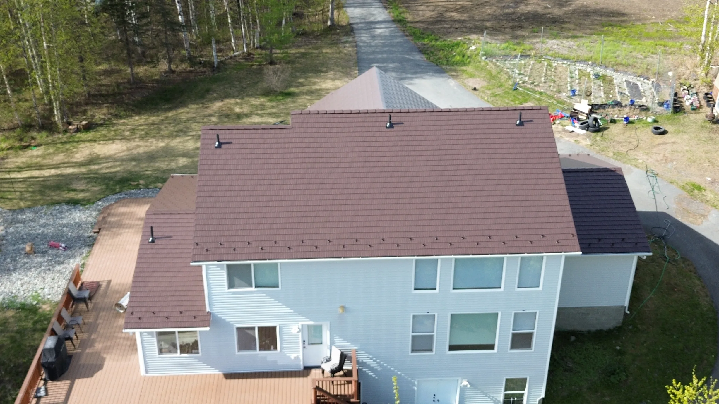 Aerial view of a colonial-style house with a brown metal roof, set amidst lush greenery and a rural landscape.