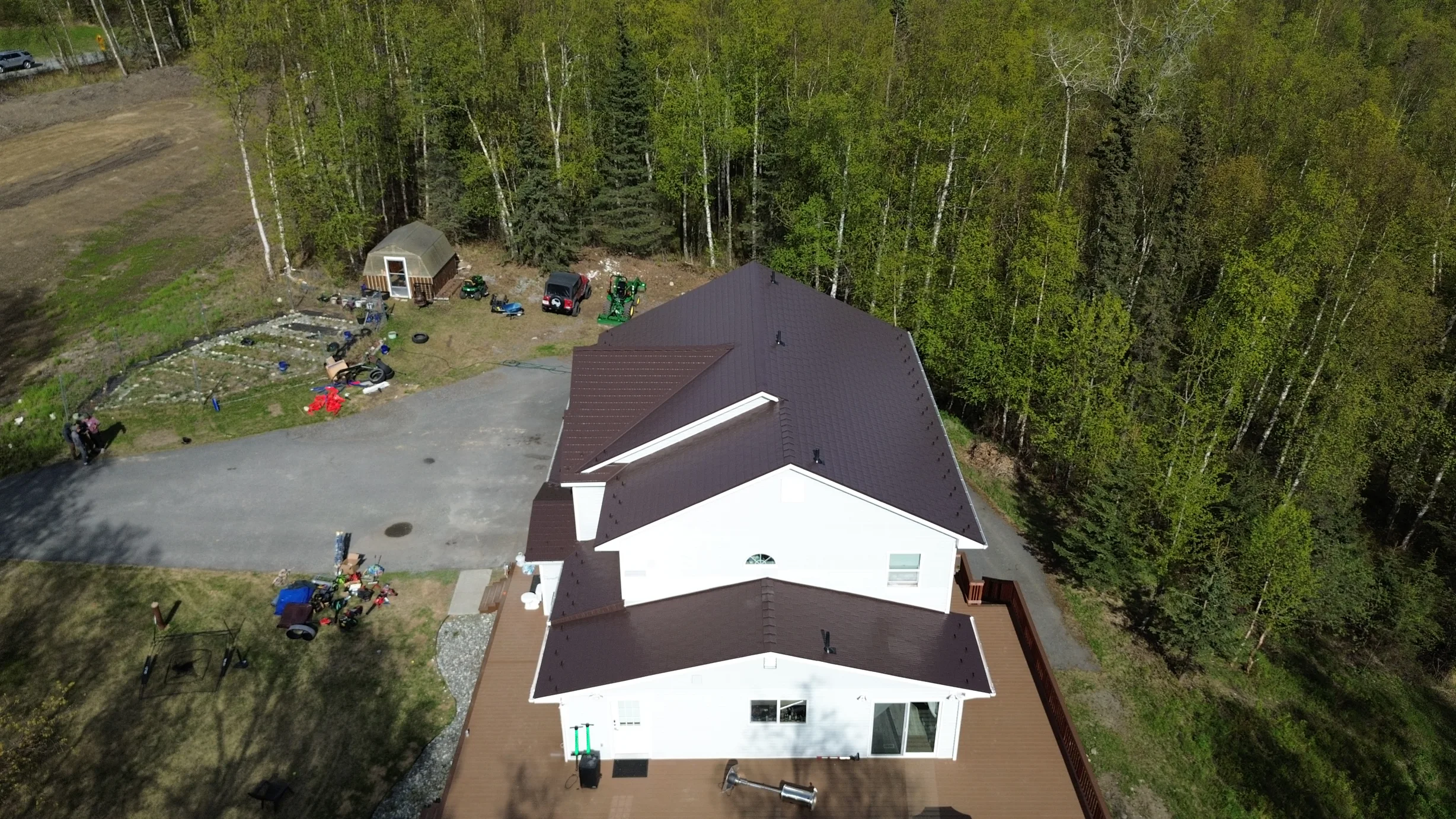 A white house with a brown metal roof in a forested, rural setting.