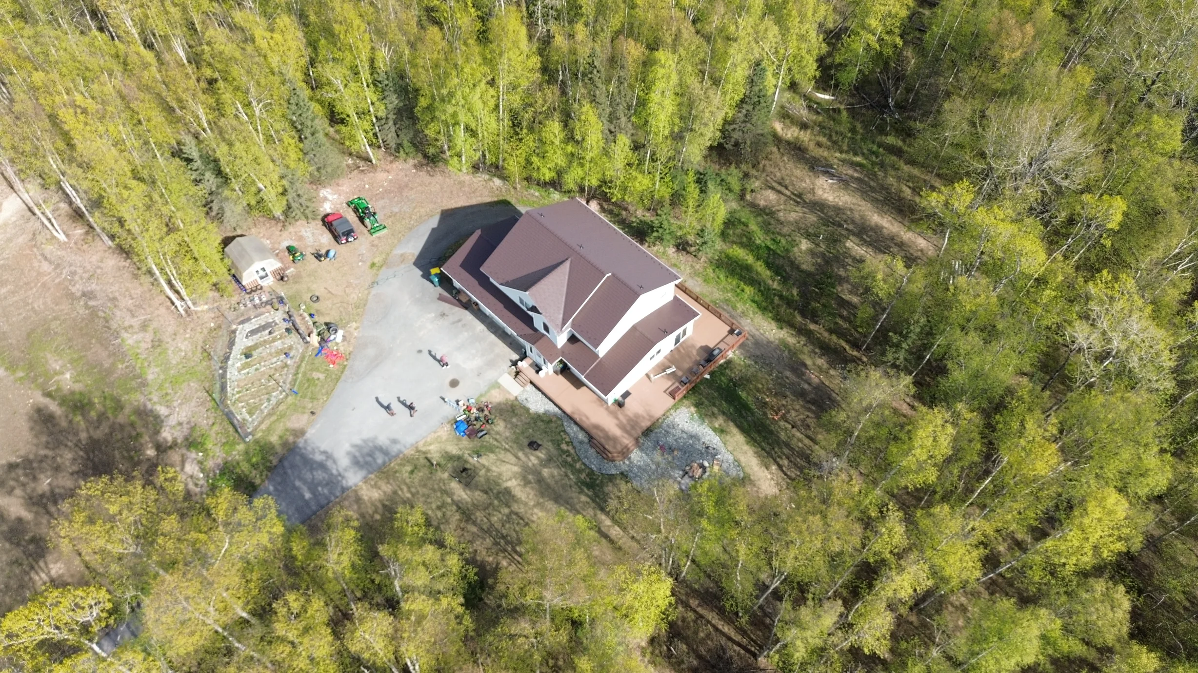 Aerial view of a ranch-style home with a brown metal roof under construction in a wooded area