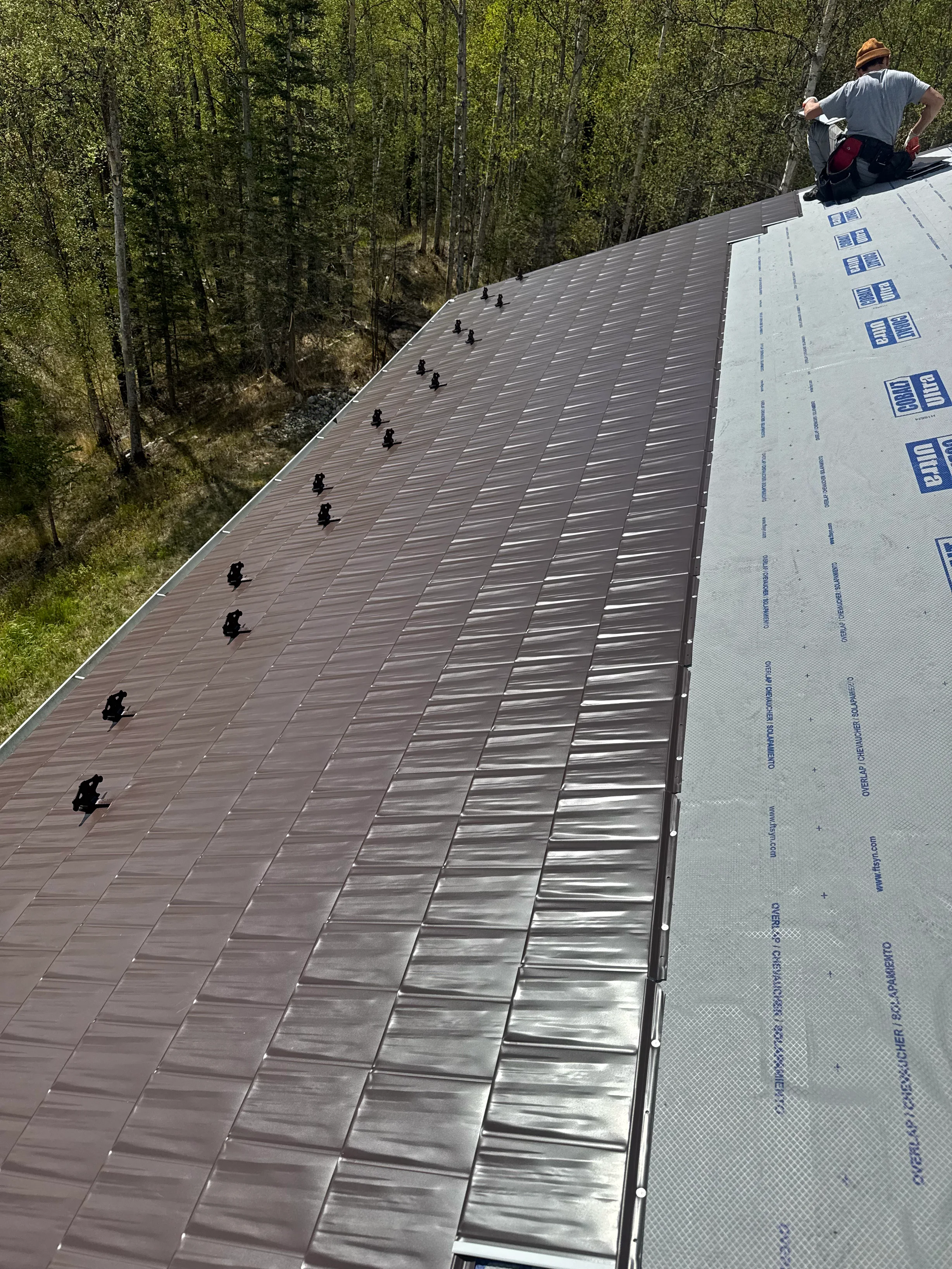 A metal roof under construction in a forested, rural area.