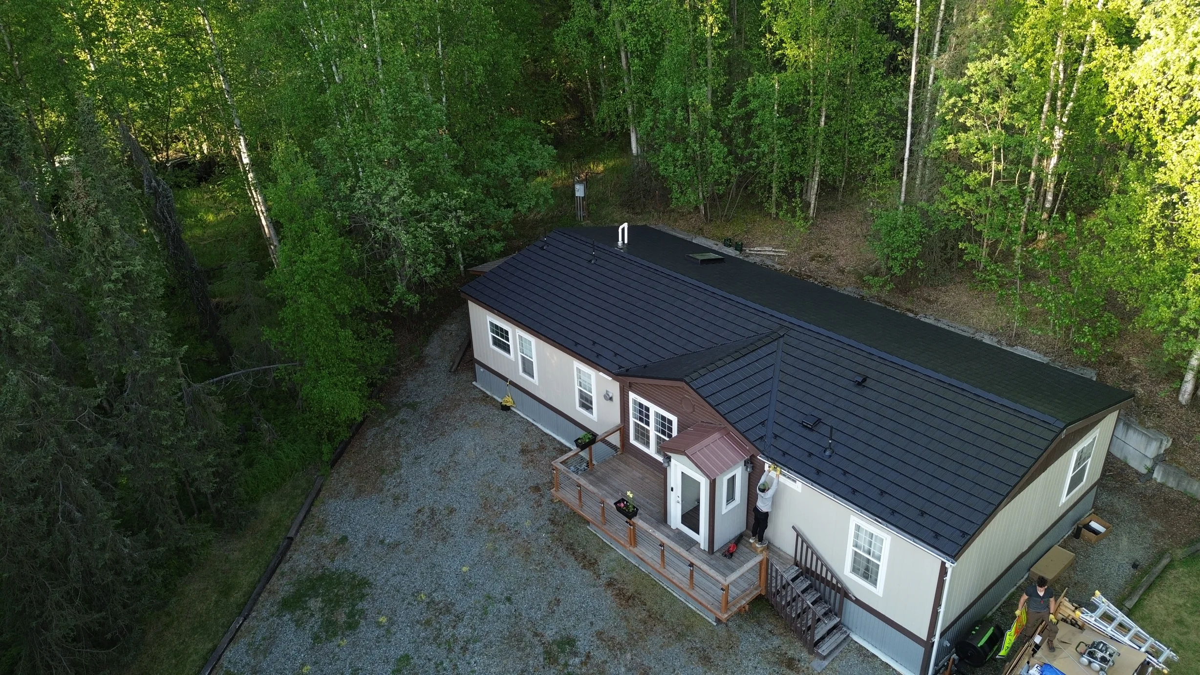 Metal roof on a ranch-style house in a forested rural area with lush greenery and a blue sky.
