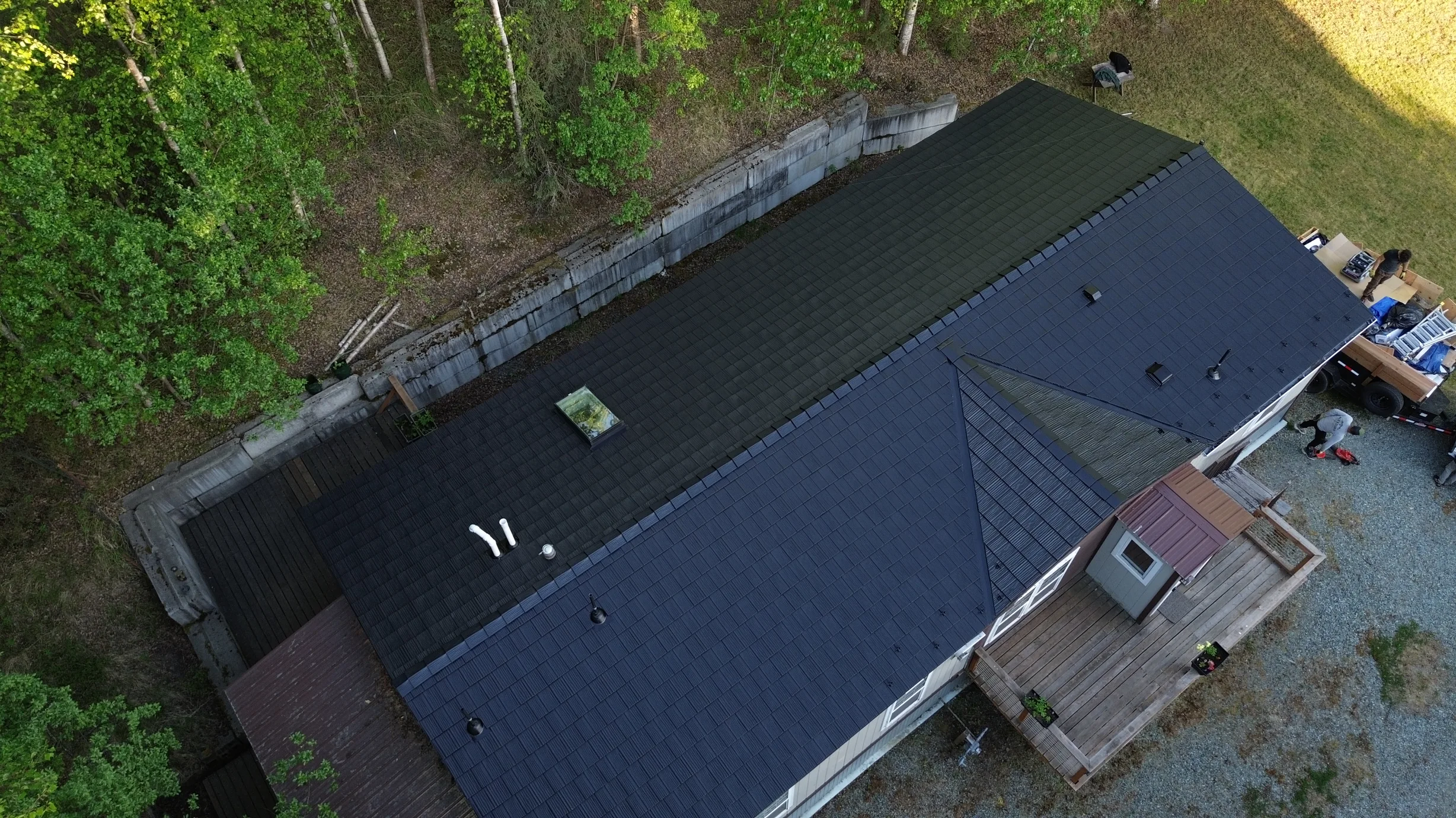 Aerial view of a modern, single-family home with a dark metal roof and solar panels in a forested rural area.
