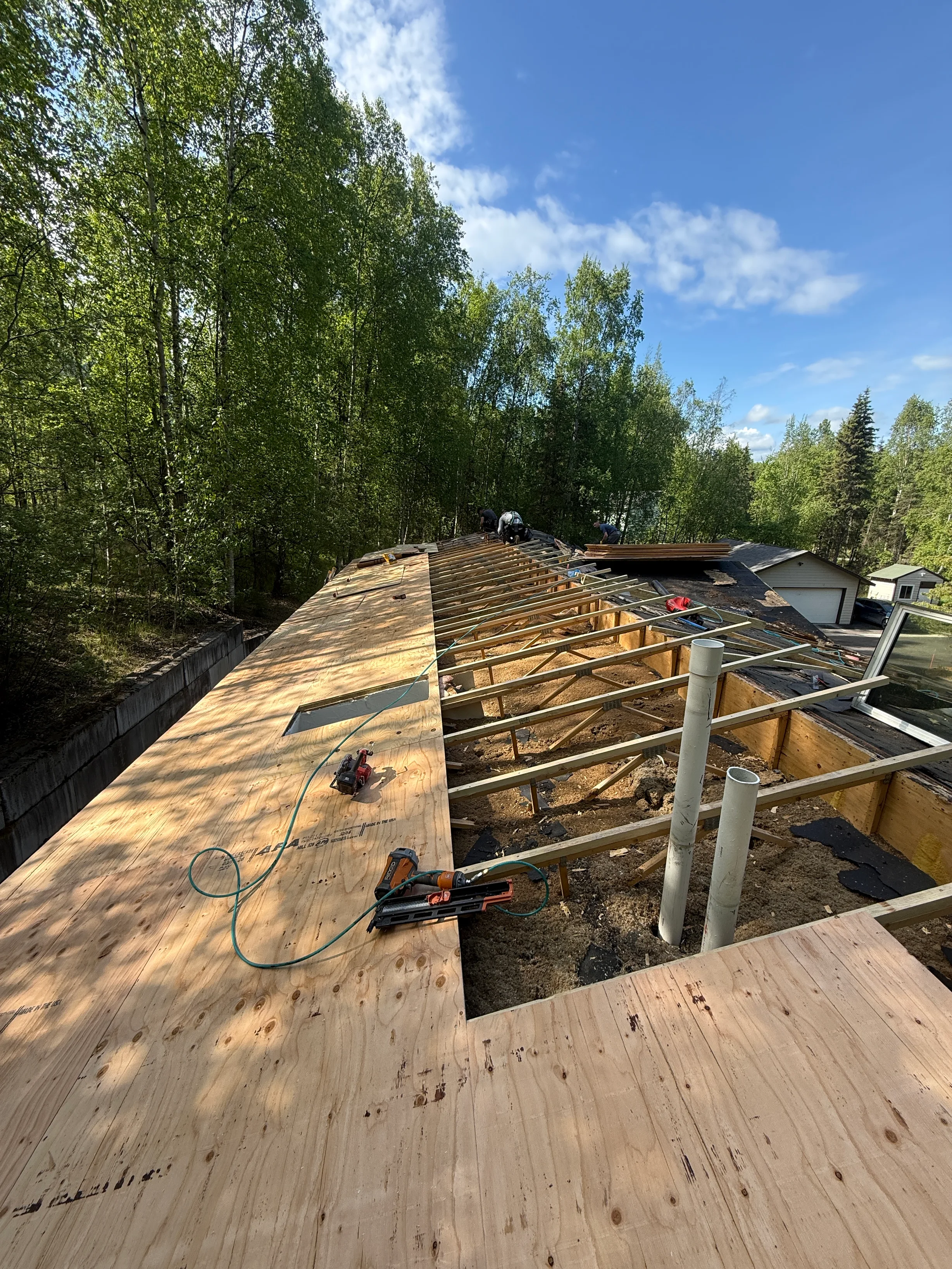 A modern metal roof being installed on a single-family home in a forested area.
