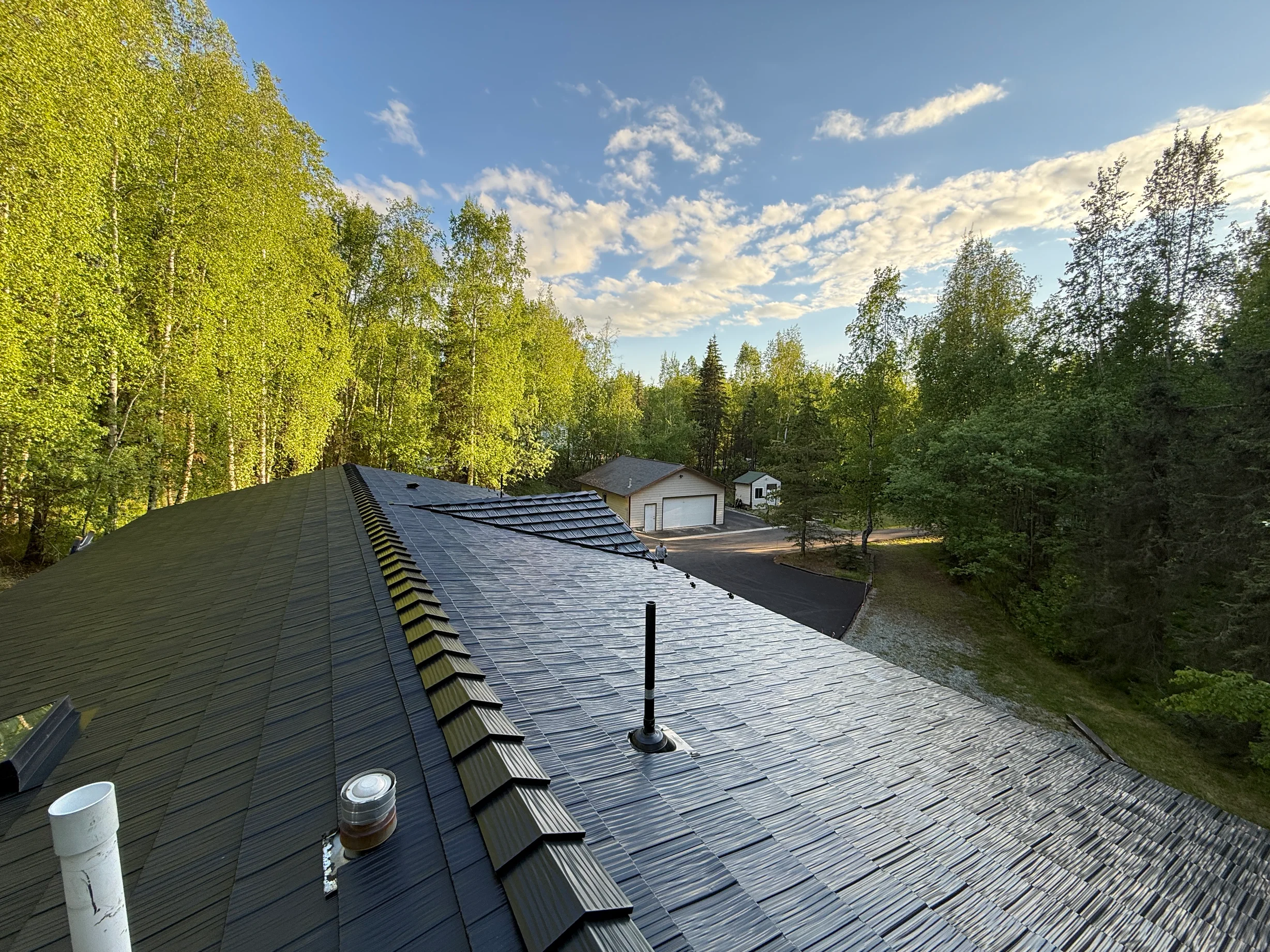 A modern metal roof installed by Interlock on a single-family home in a forested area with lush greenery and a blue sky.