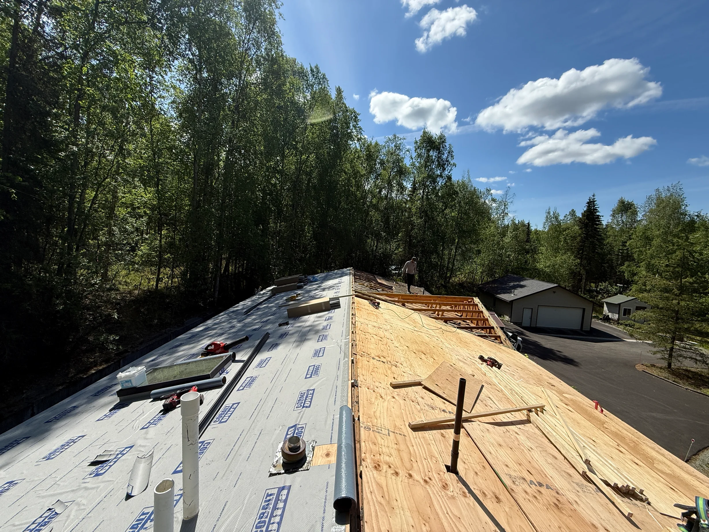 A modern-style home with a metal roof under construction in a forested rural area.