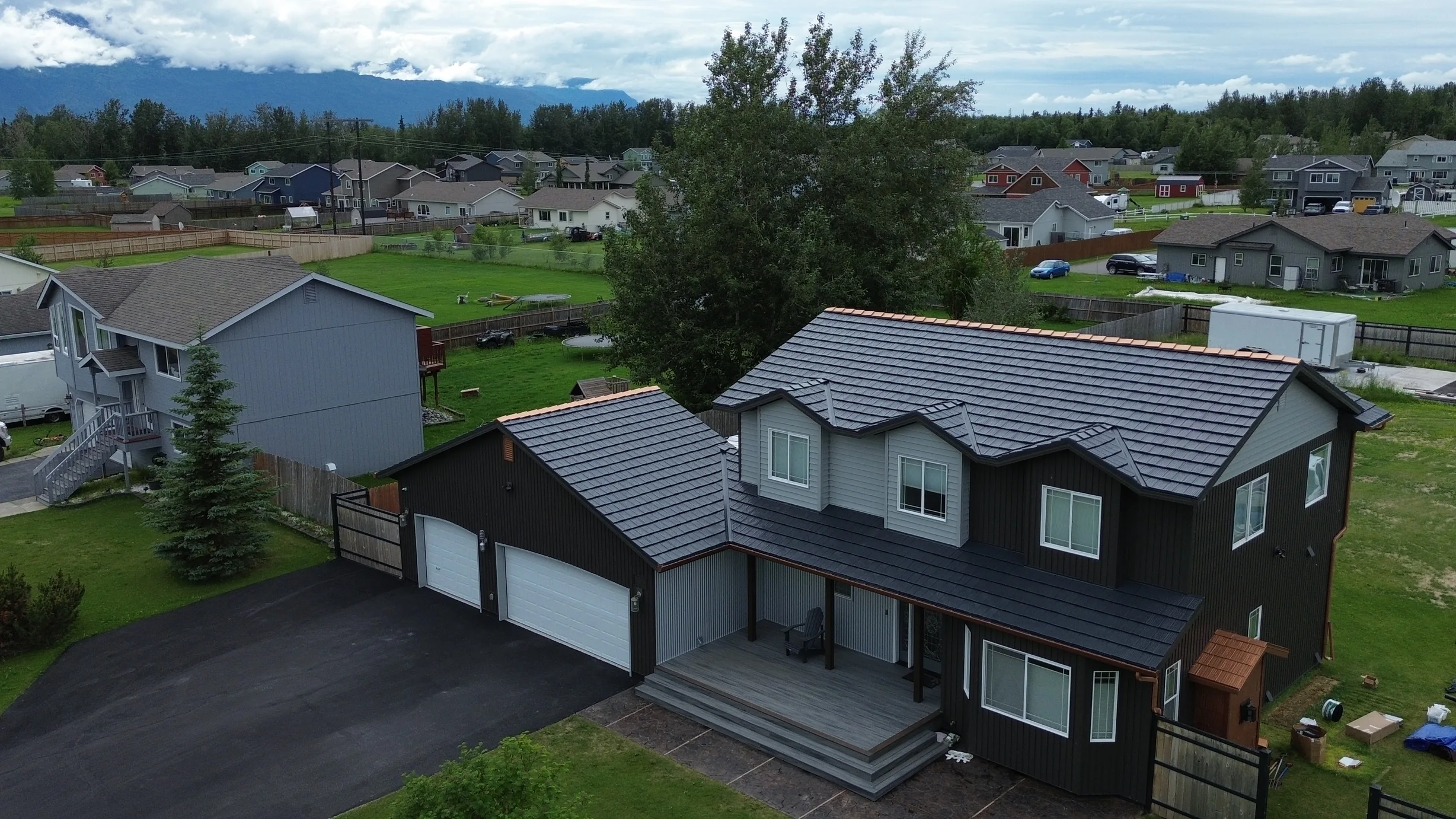 A modern single-family home with a metal roof in a suburban area surrounded by lush greenery and a blue sky.