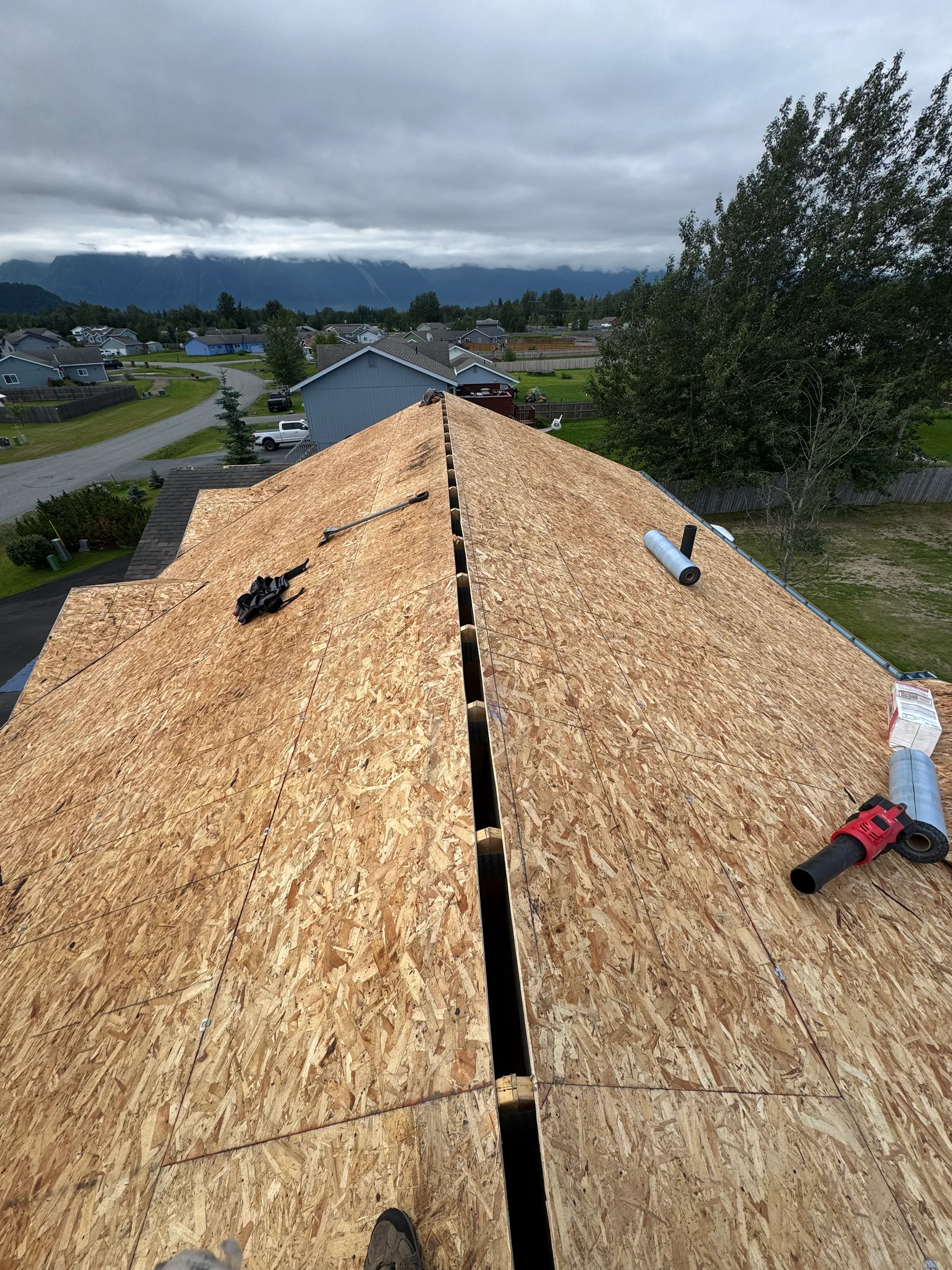 A metal roof under construction on a rural home with a mountainous backdrop.