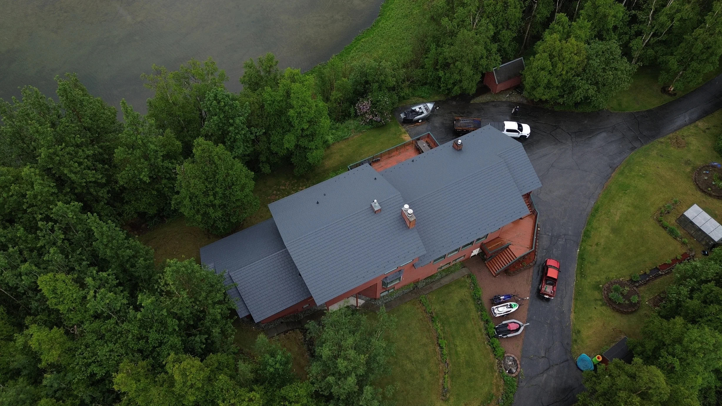 A ranch-style home with a grey metal roof and brown brick exterior, surrounded by trees and greenery.