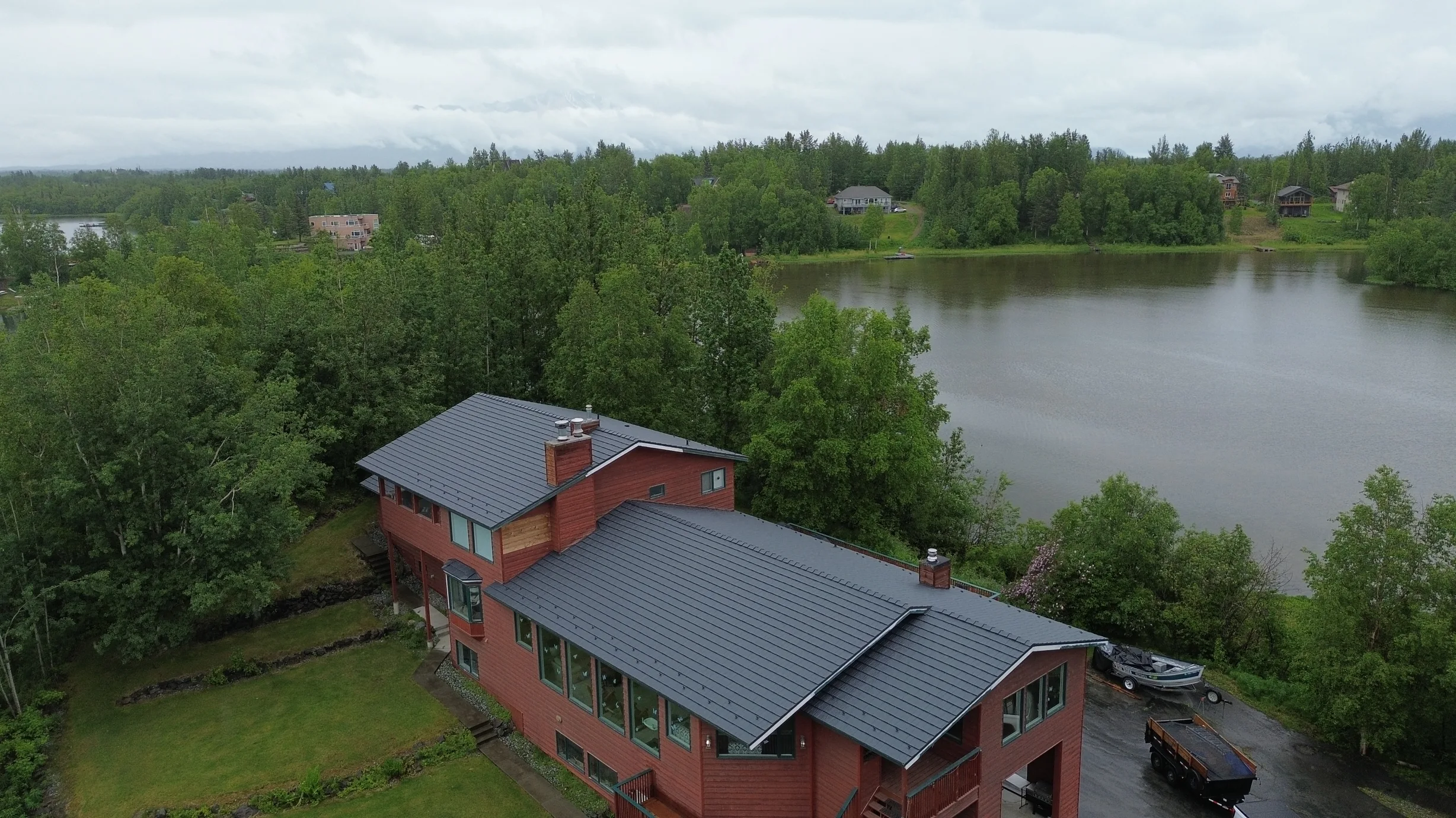 Aerial view of a red modern home with a grey metal roof overlooking a lake.