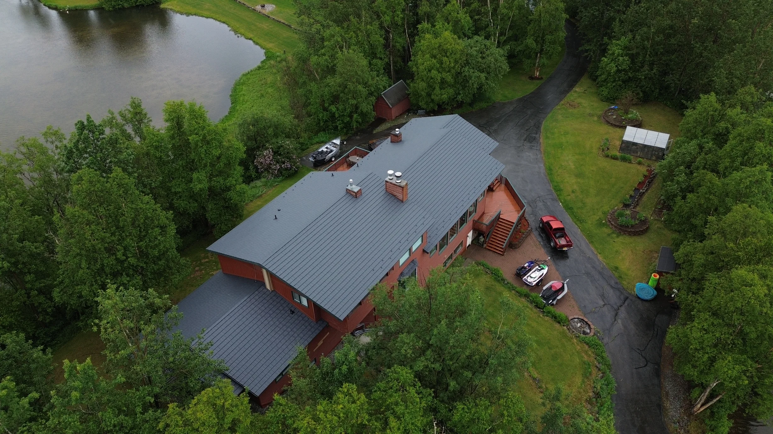 A ranch-style home with a red metal roof, set against a backdrop of lush greenery and a serene lakeside setting.