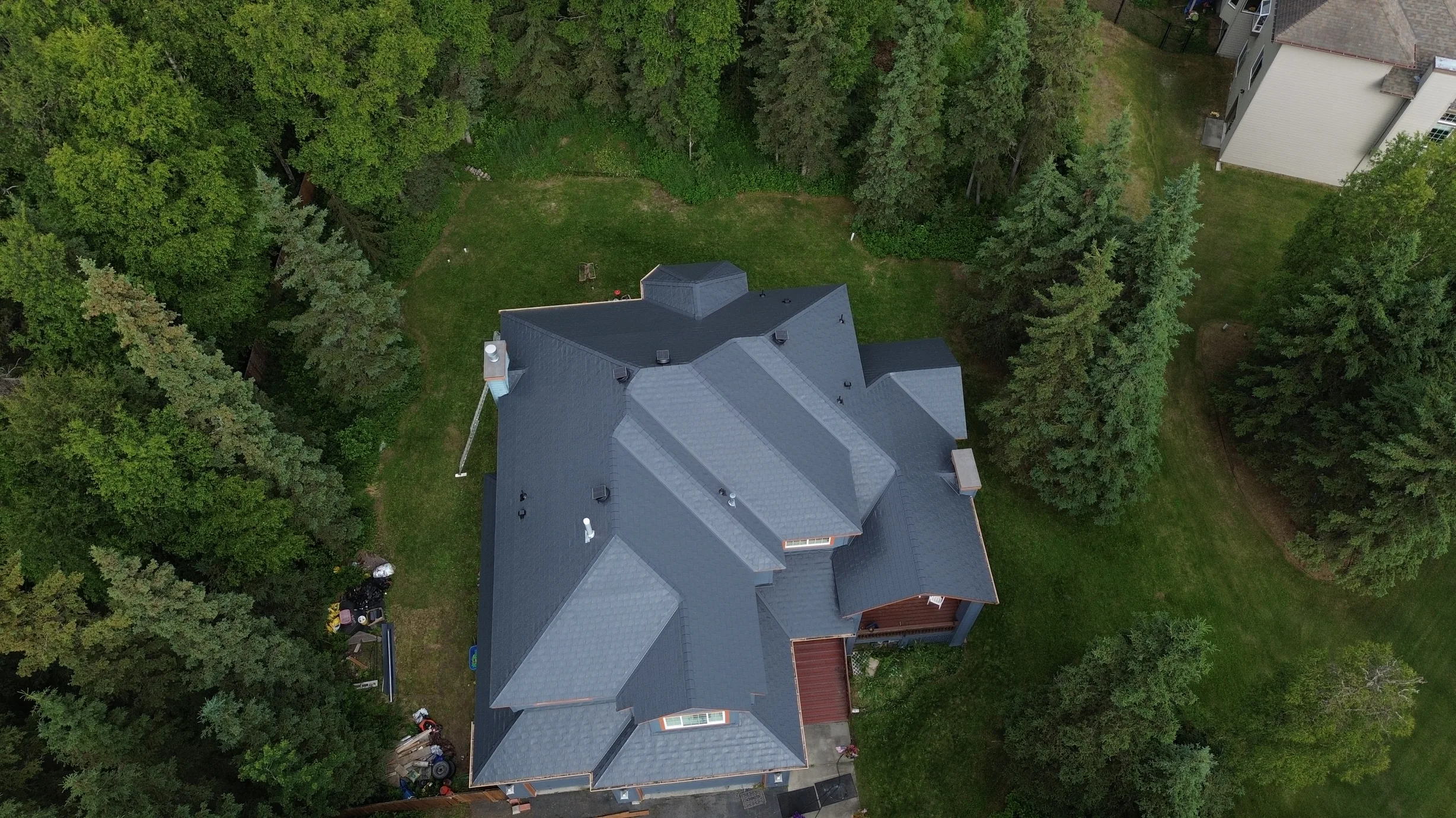 Aerial view of a modern single-family home with a grey metal roof, surrounded by lush greenery and set in a rural forested area.