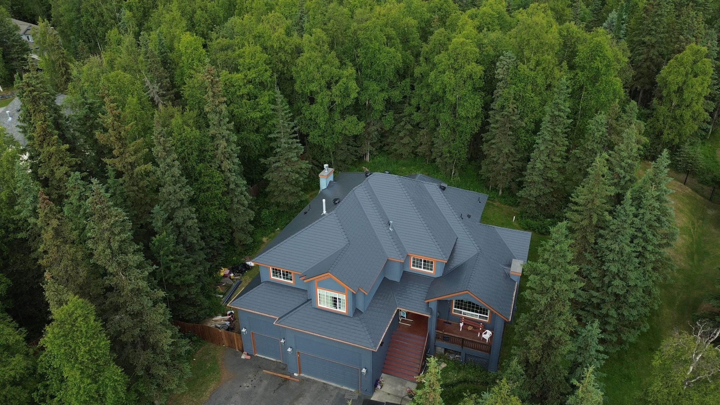 A modern home with a blue metal roof and brown trim in a forested rural setting.