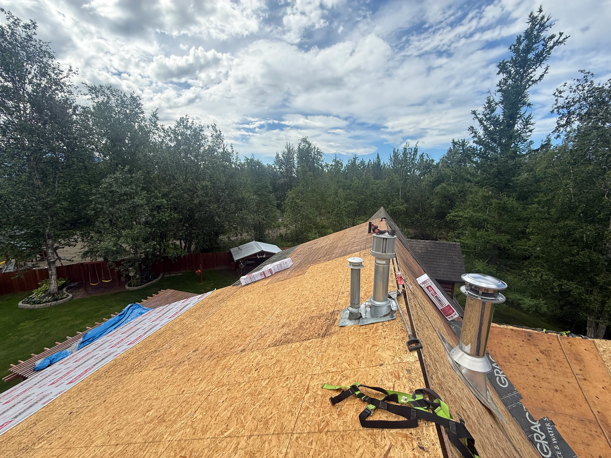 A metal roof installation in progress on a single-family home in a forested rural area with a blue sky