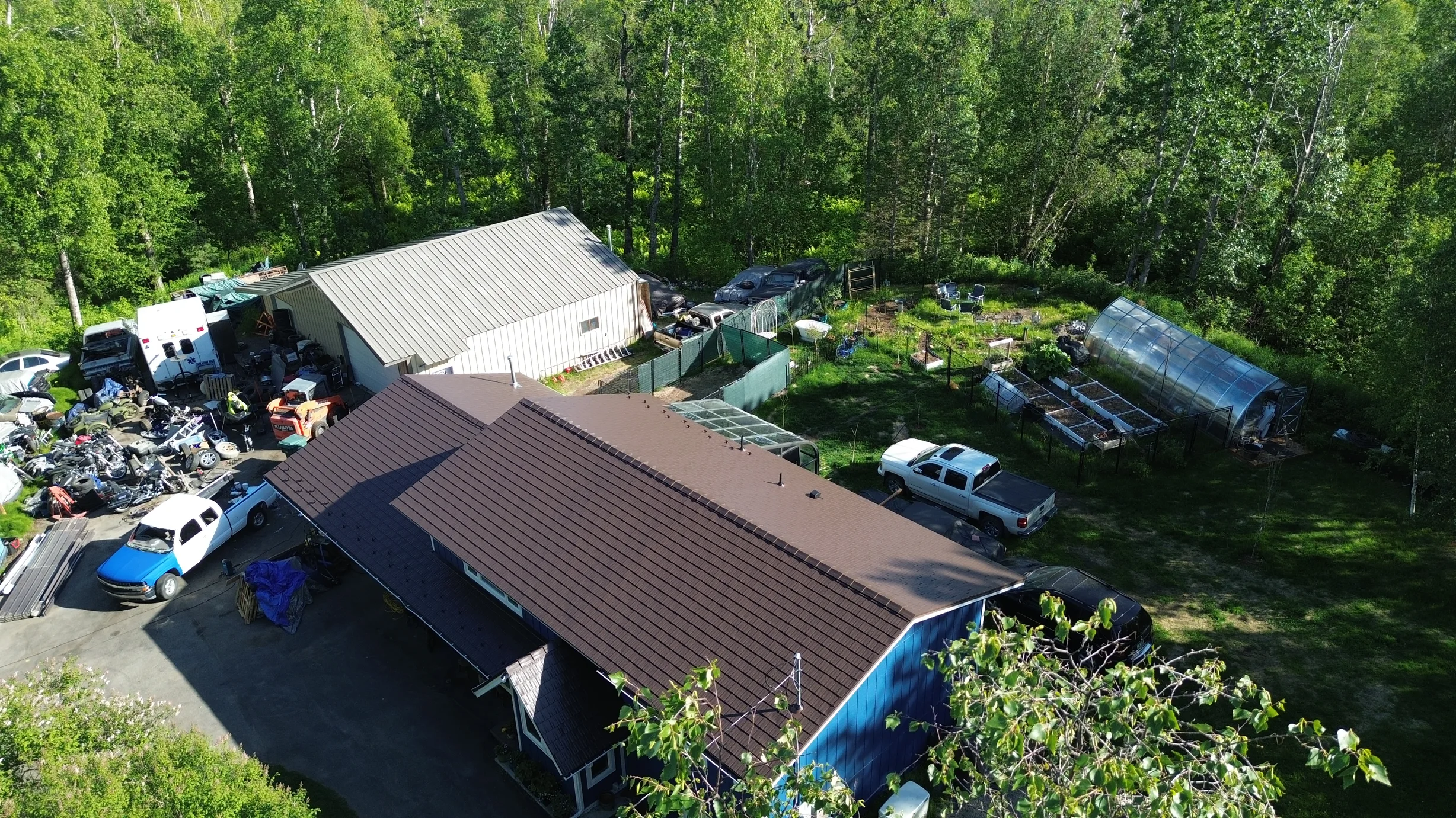 Aerial view of a house with a brown metal roof, surrounded by lush greenery