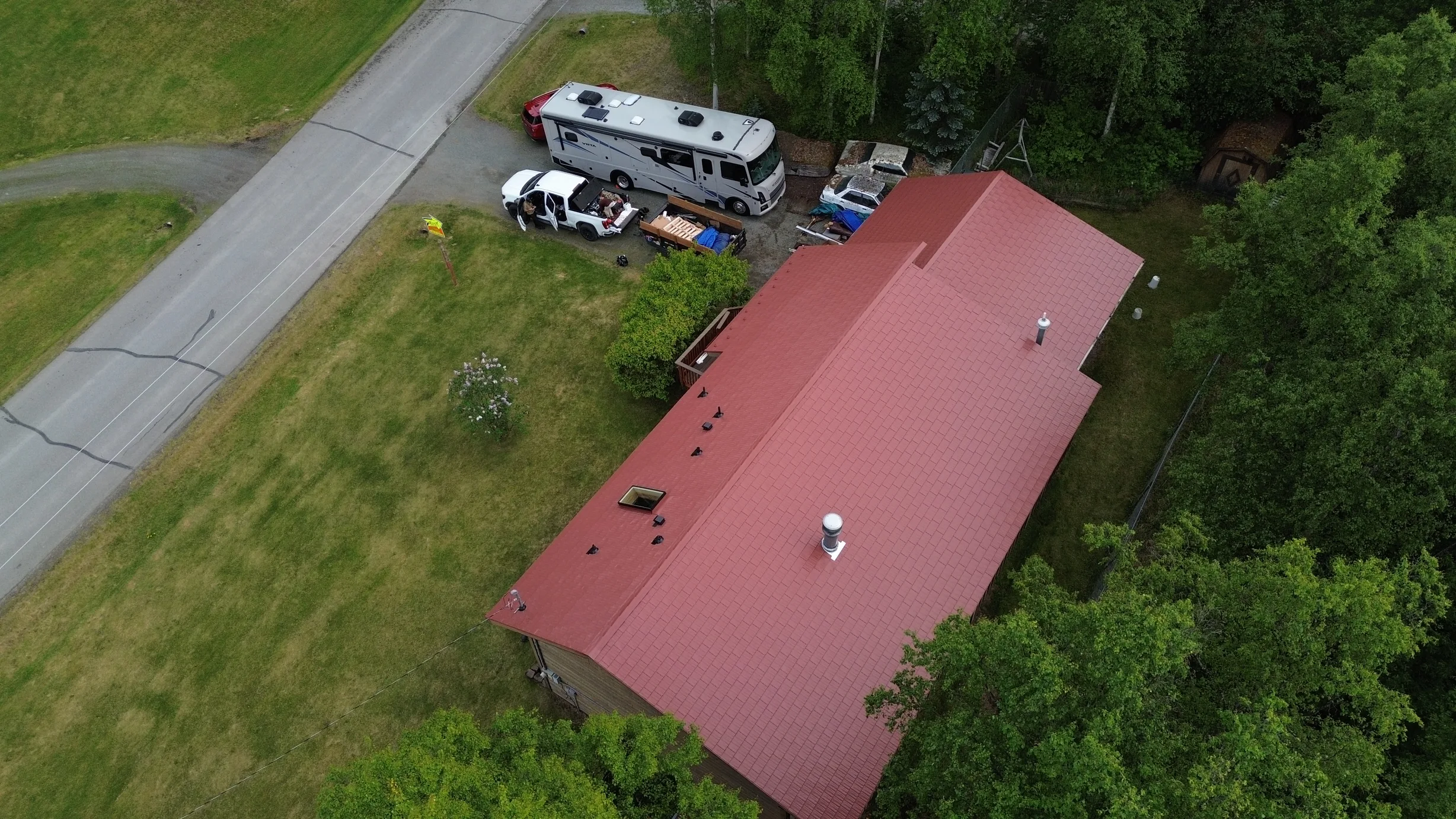 A ranch style house with a red metal roof and a white RV parked in the driveway.