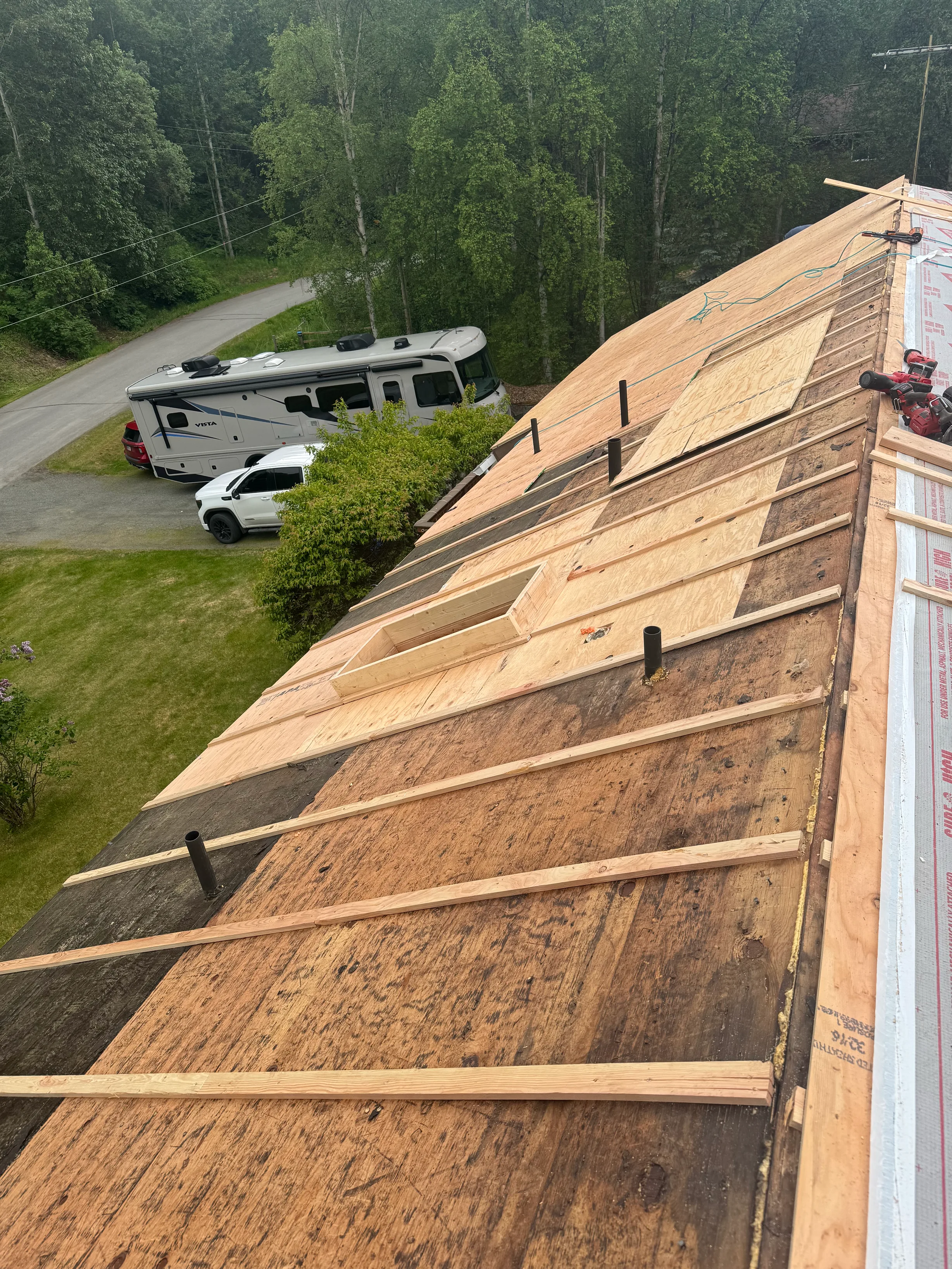 A metal roof under construction with snow guards and ridge cap in a forested rural area
