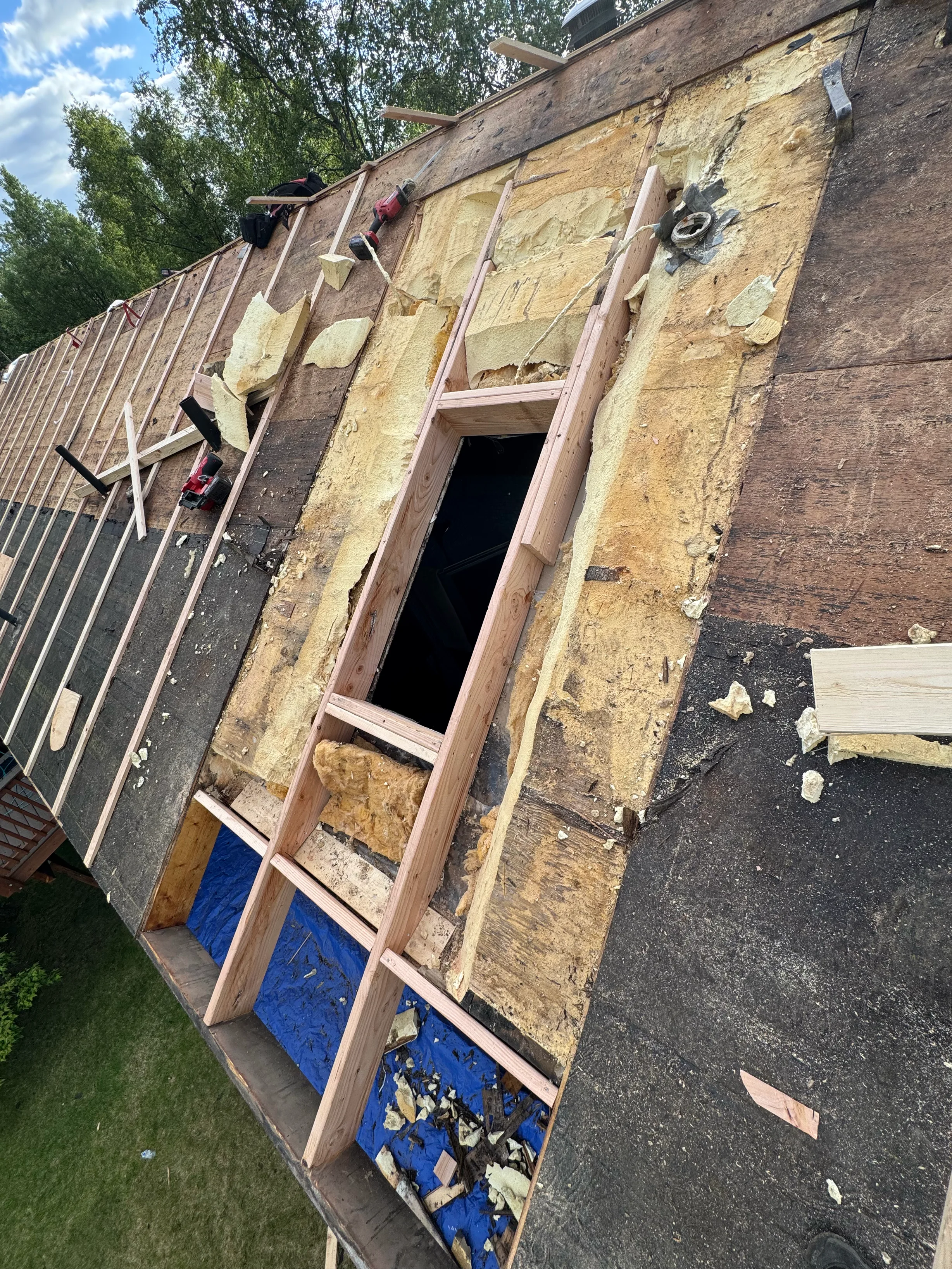 A metal roof being installed on a house in a forested urban area with lush greenery.
