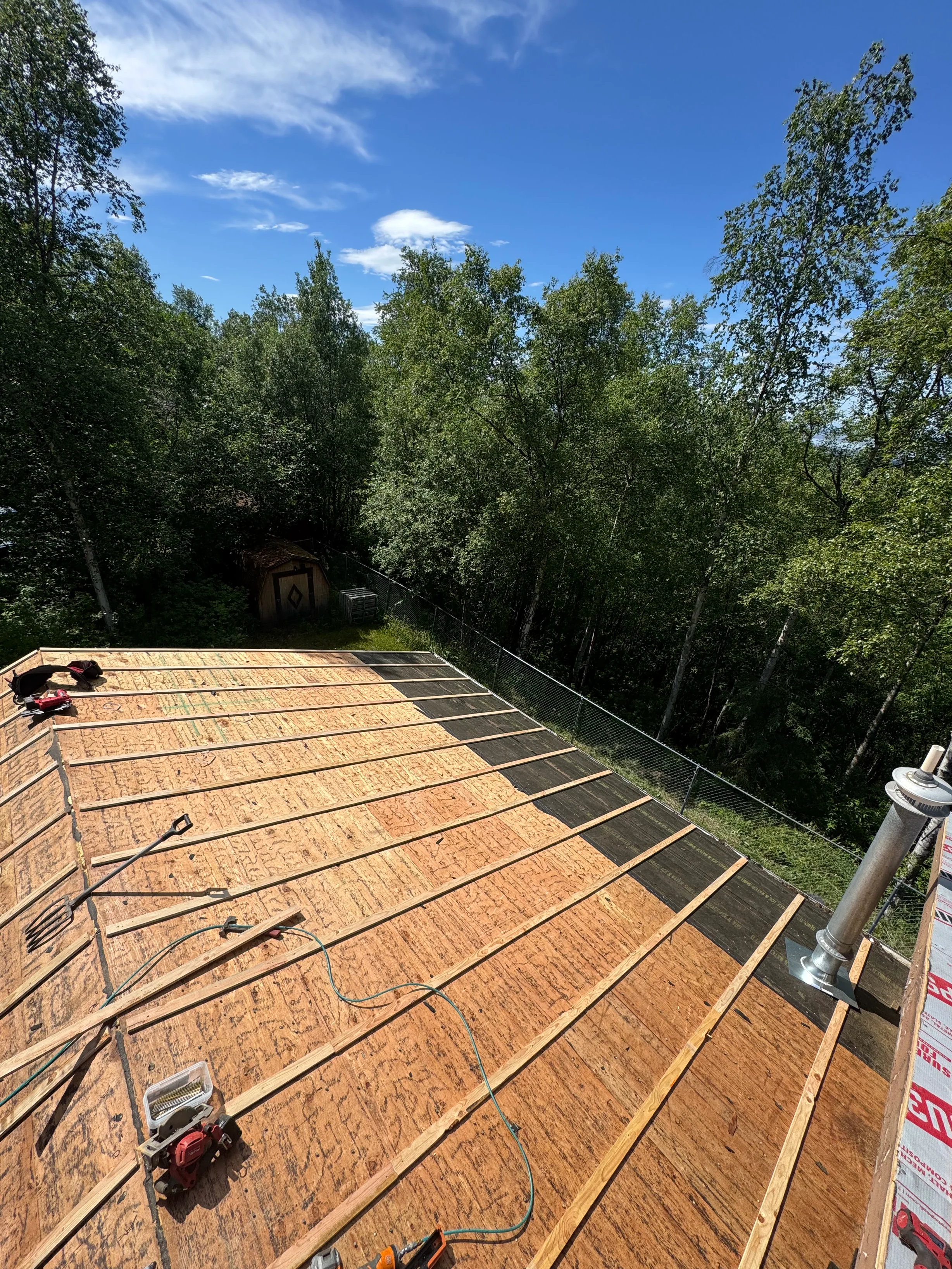 A modern house with a metal roof under construction in a forested rural setting