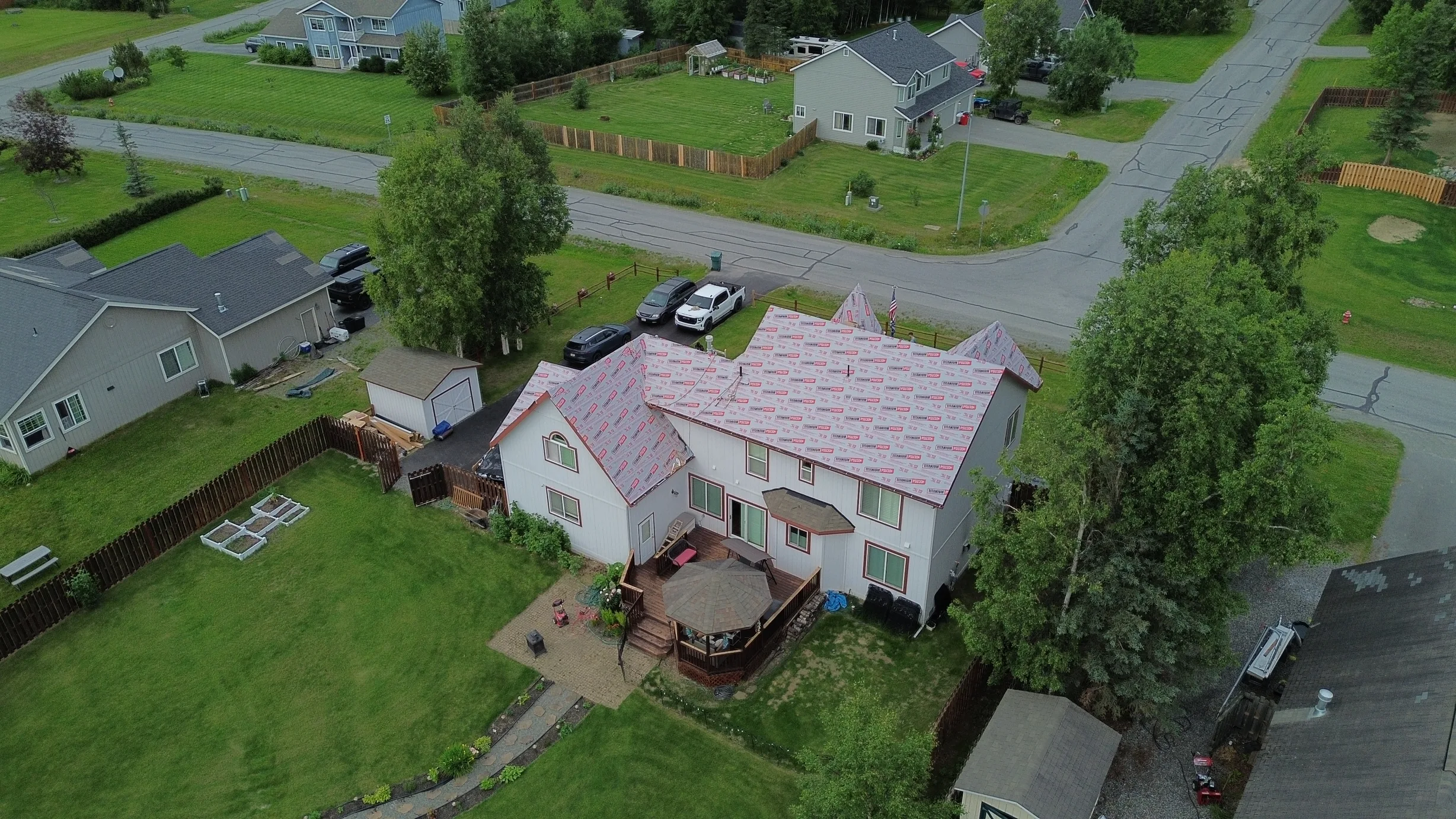 Aerial view of a colonial-style home with a pink metal roof in a rural setting, surrounded by lush greenery and a blue sky