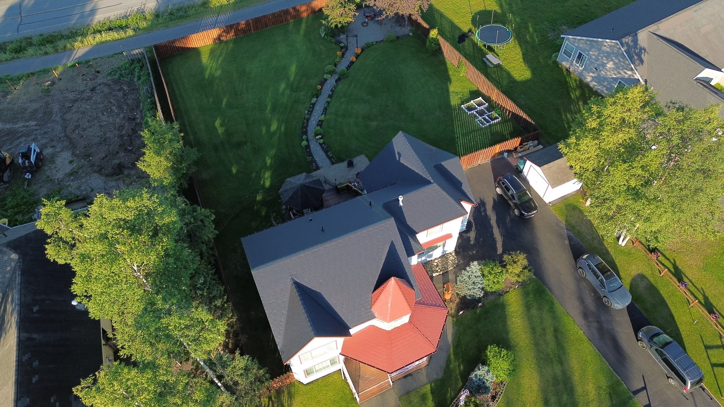 A colonial-style home with a dark grey metal roof and red trim, surrounded by lush greenery and a blue sky.