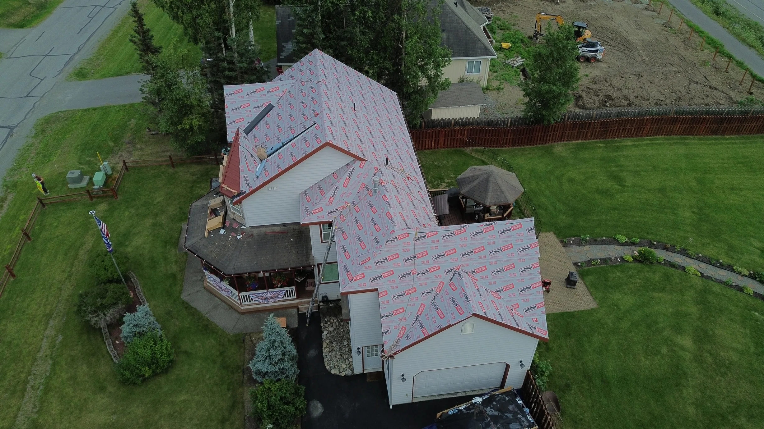 Aerial view of a metal roof being installed on a ranch-style single-family home in a suburban area with lush greenery.