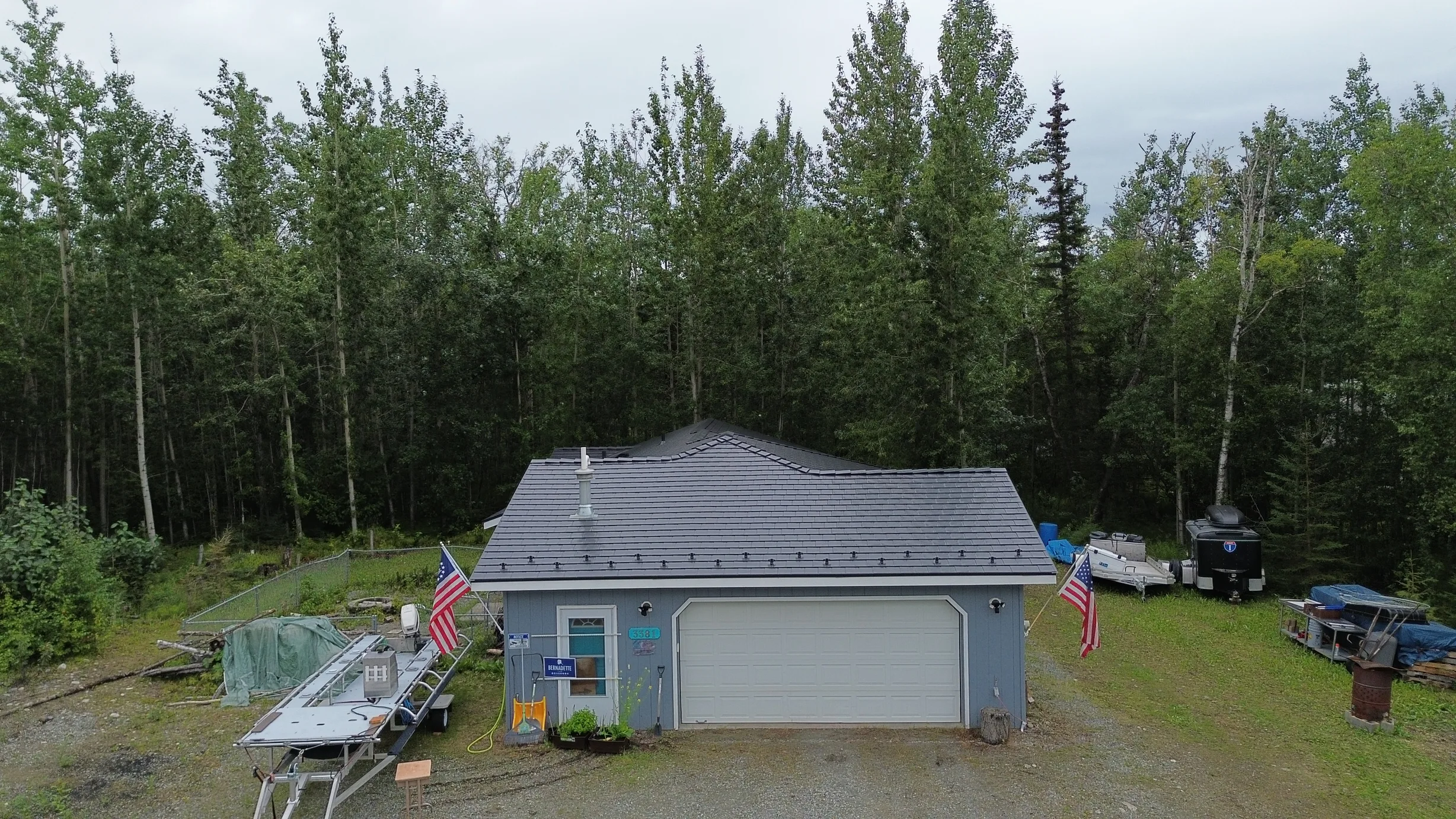 A ranch-style home with a metal roof and lush greenery, located in a forested rural area.