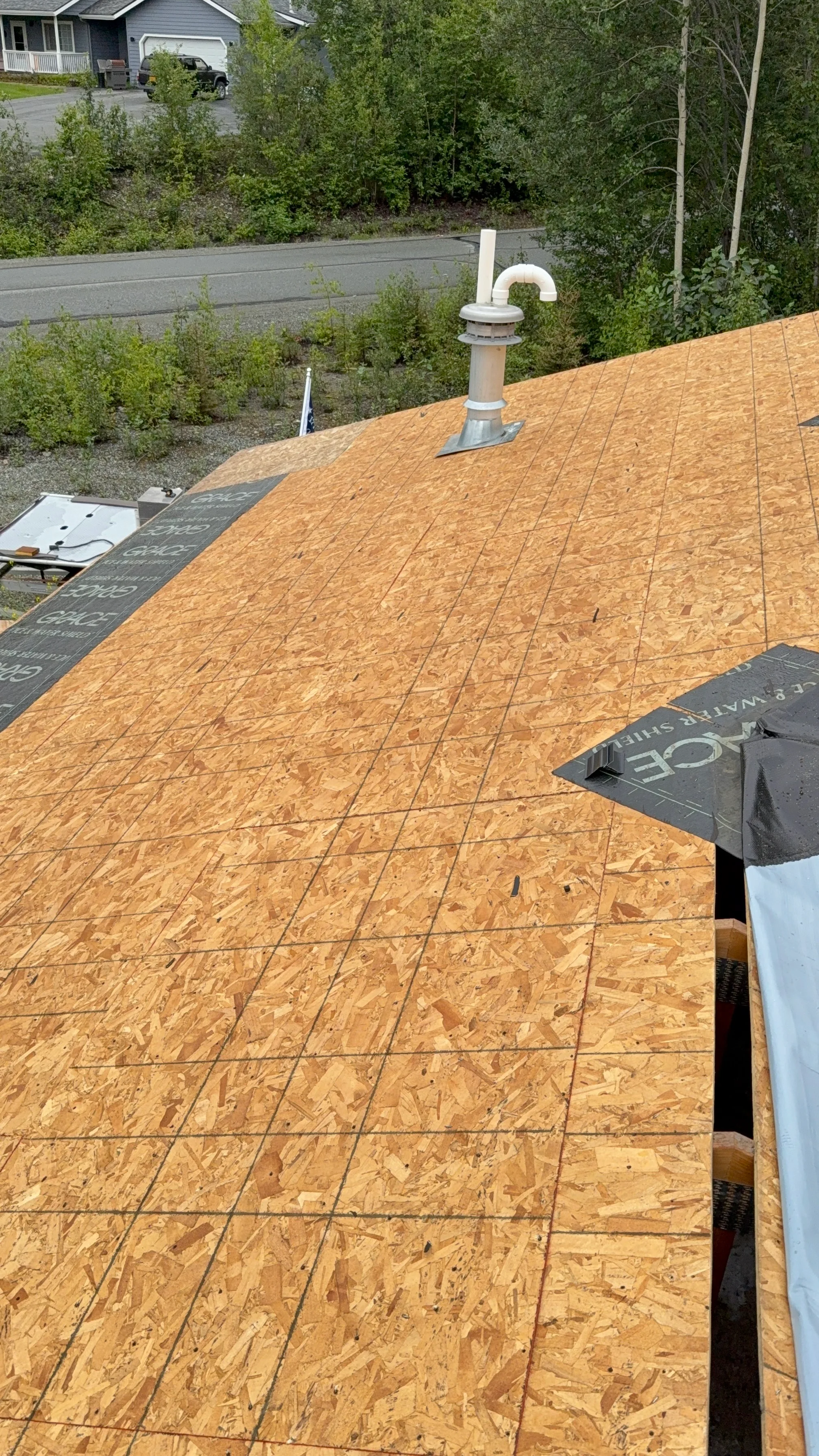 A modern home with a new metal roof installation in progress, surrounded by lush greenery.