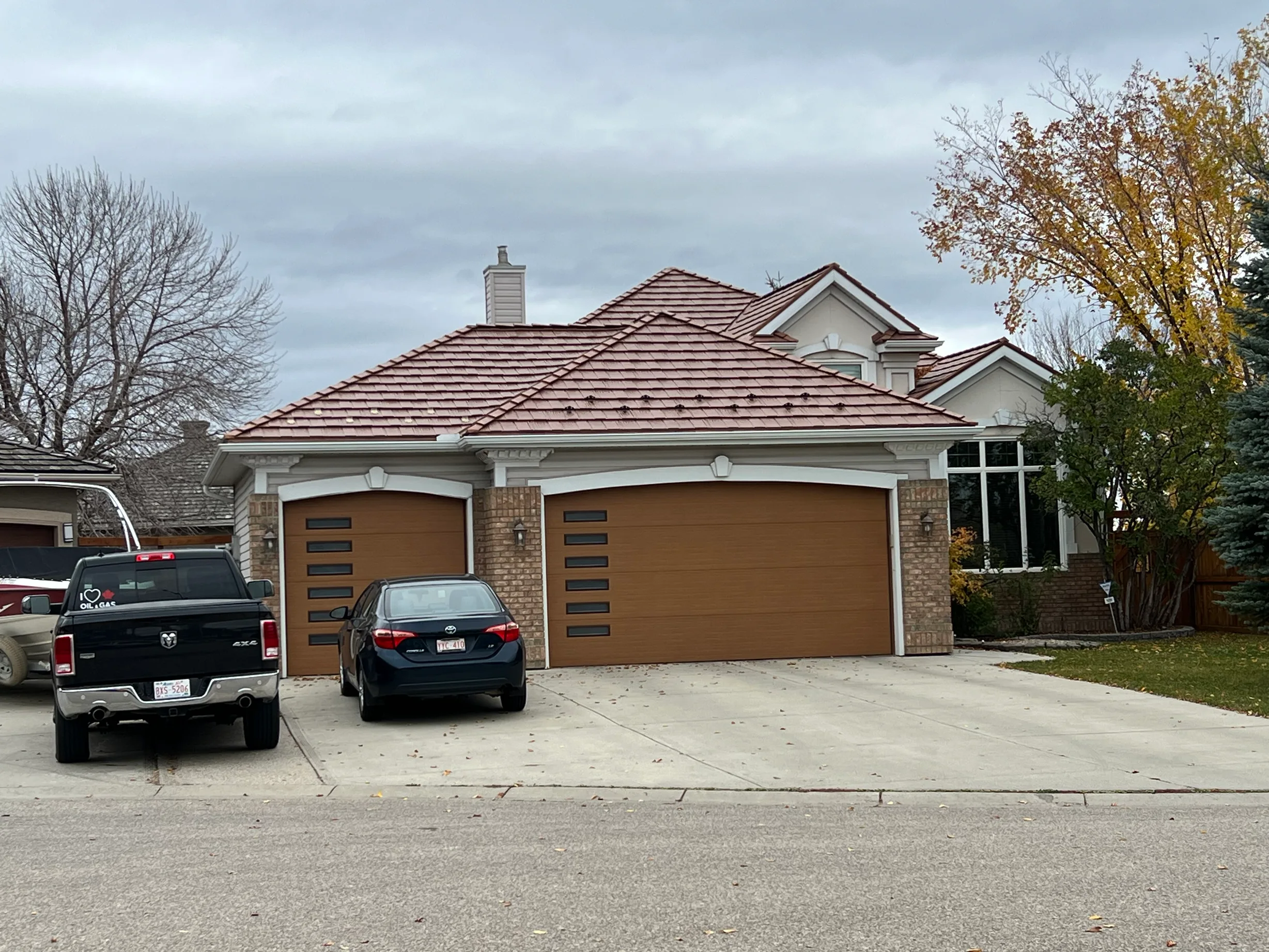 Aged Copper Interlock Shake aluminum roof on a beige ranch house with brown garage doors among trees, Calgary, Alberta