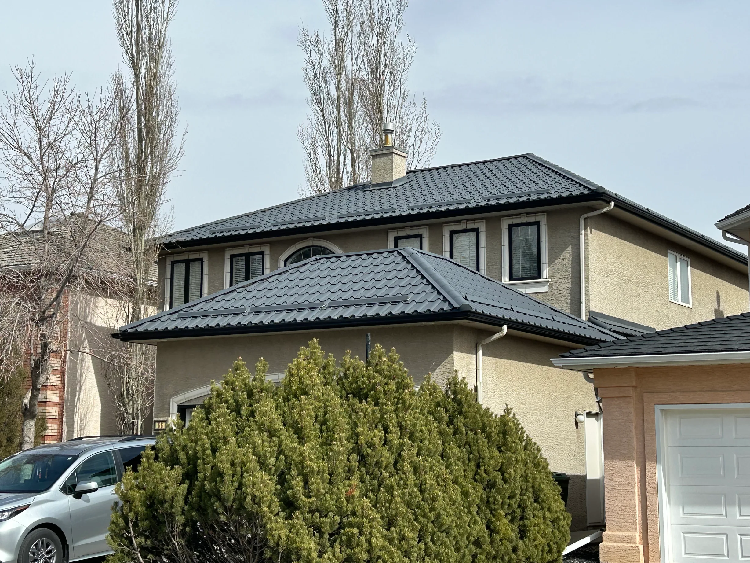 Charcoal Grey Interlock Tile aluminum roof on a tan one-storey home with solar panels and snow guards, Calgary, Alberta
