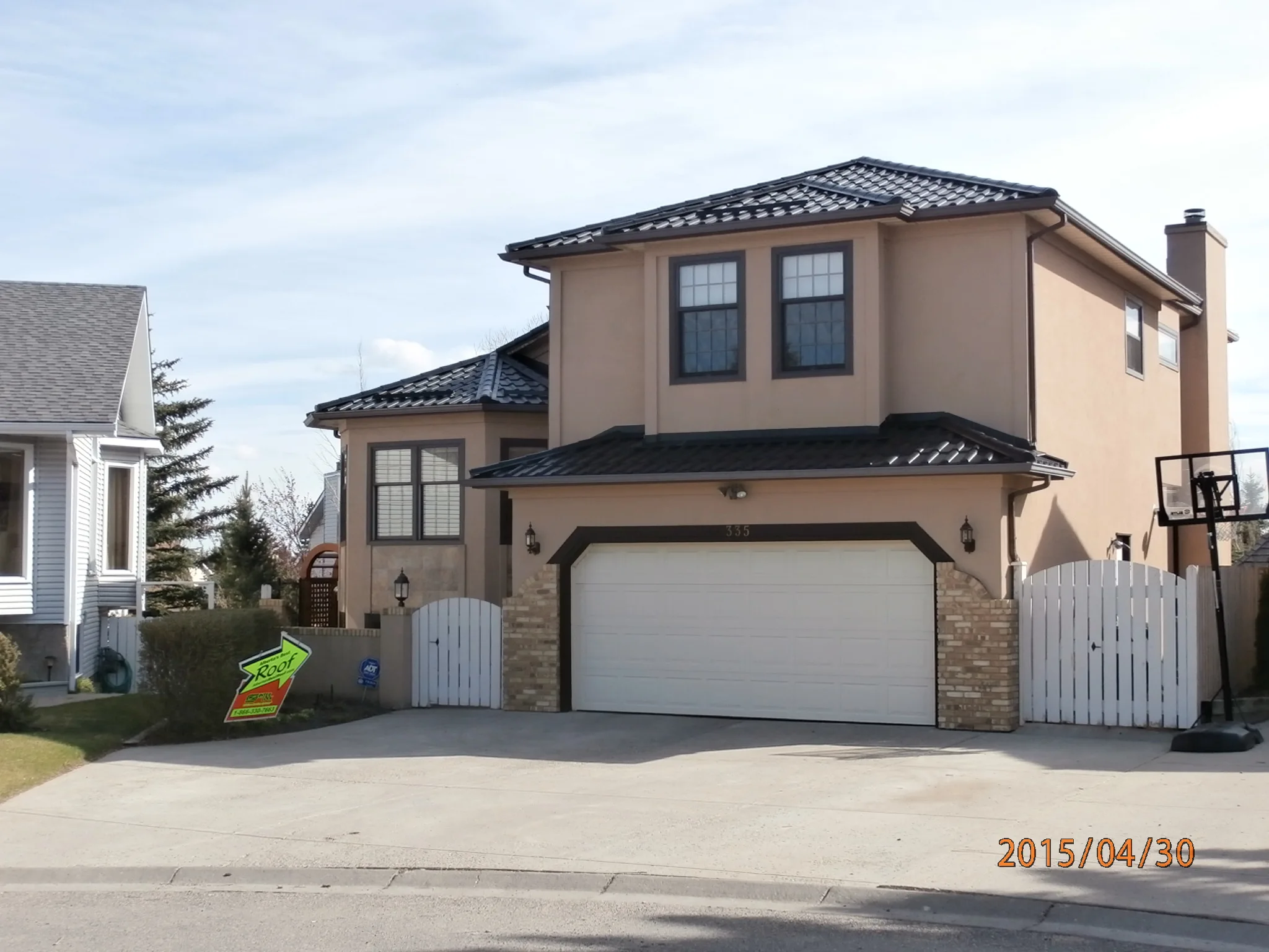 Black Interlock Tile aluminum roof on a beige two-storey home with a metal roof and a white fence, Calgary, Alberta