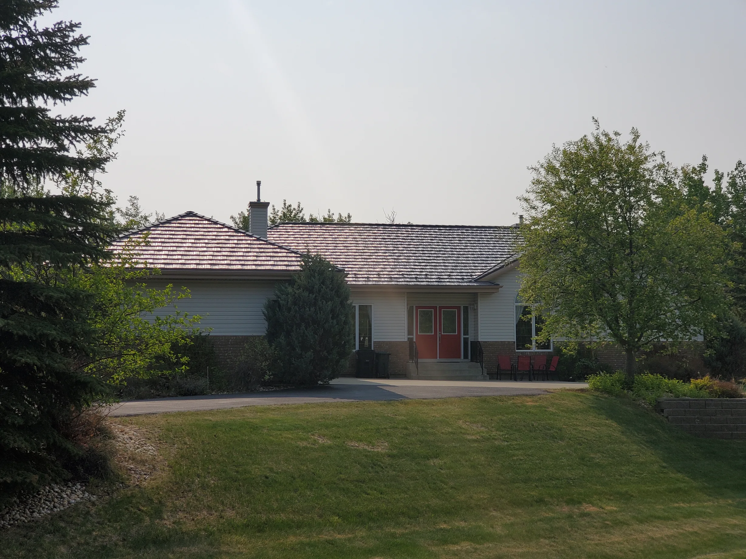 Weathered Interlock Shake aluminum roof on a white ranch home with a red door among tall trees, Sherwood Park, Alberta