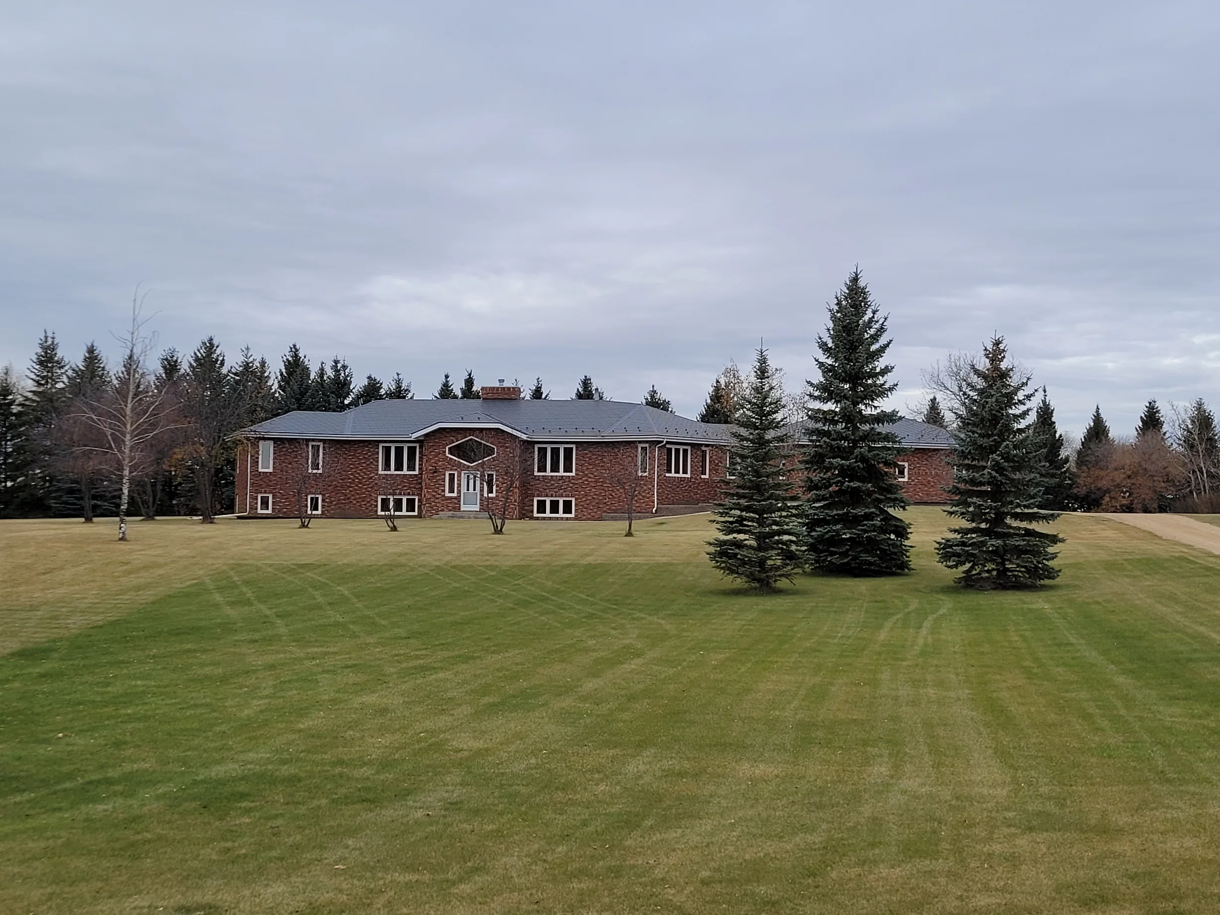 Deep Charcoal Interlock Slate aluminum roof on a red brick home with a grey metal roof in a forest clearing, Westlock, Alberta