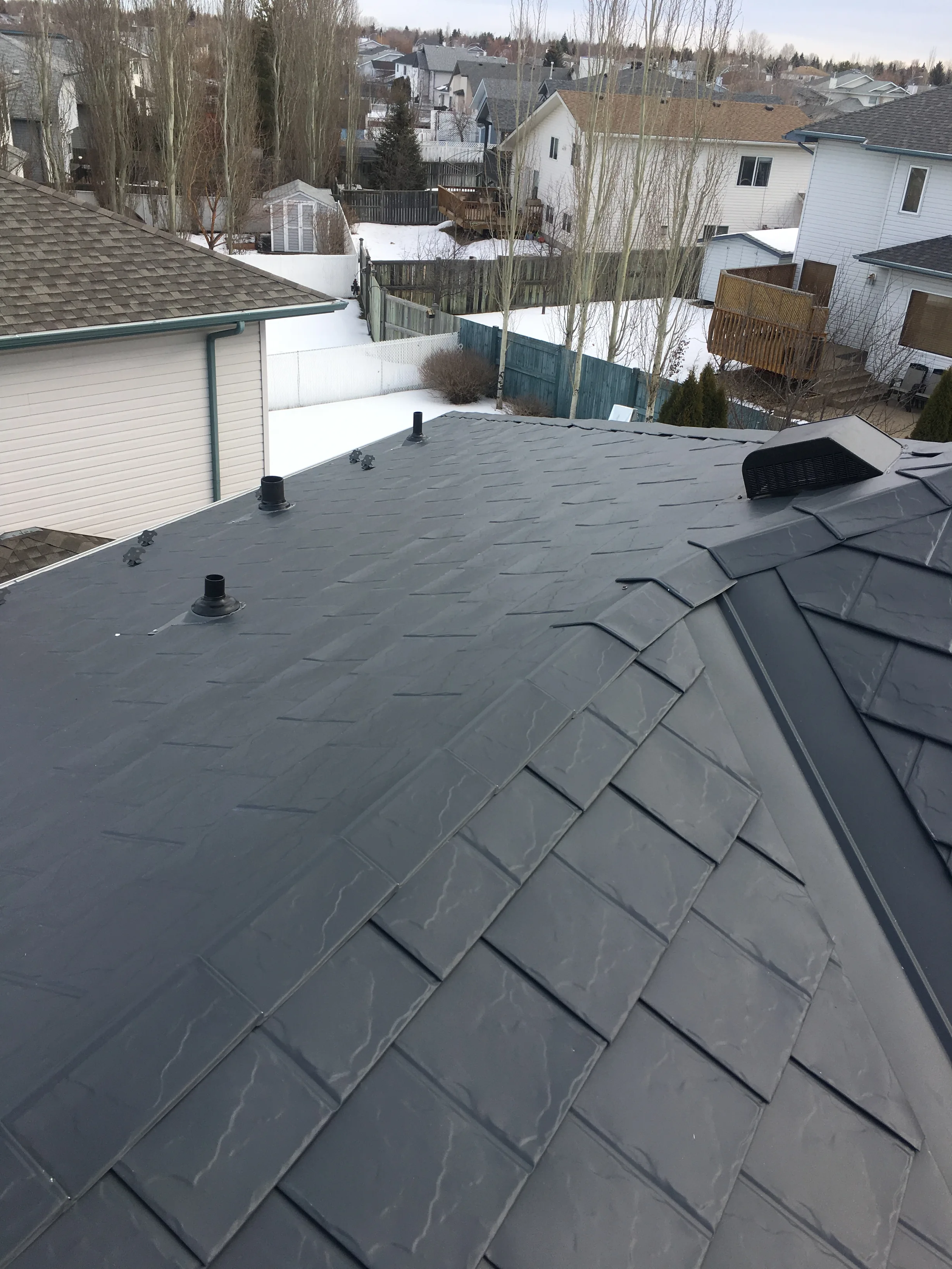 Deep Charcoal Interlock Slate aluminum roof on a white single-storey home with dormers among tall trees, Fort Saskatchewan, Alberta