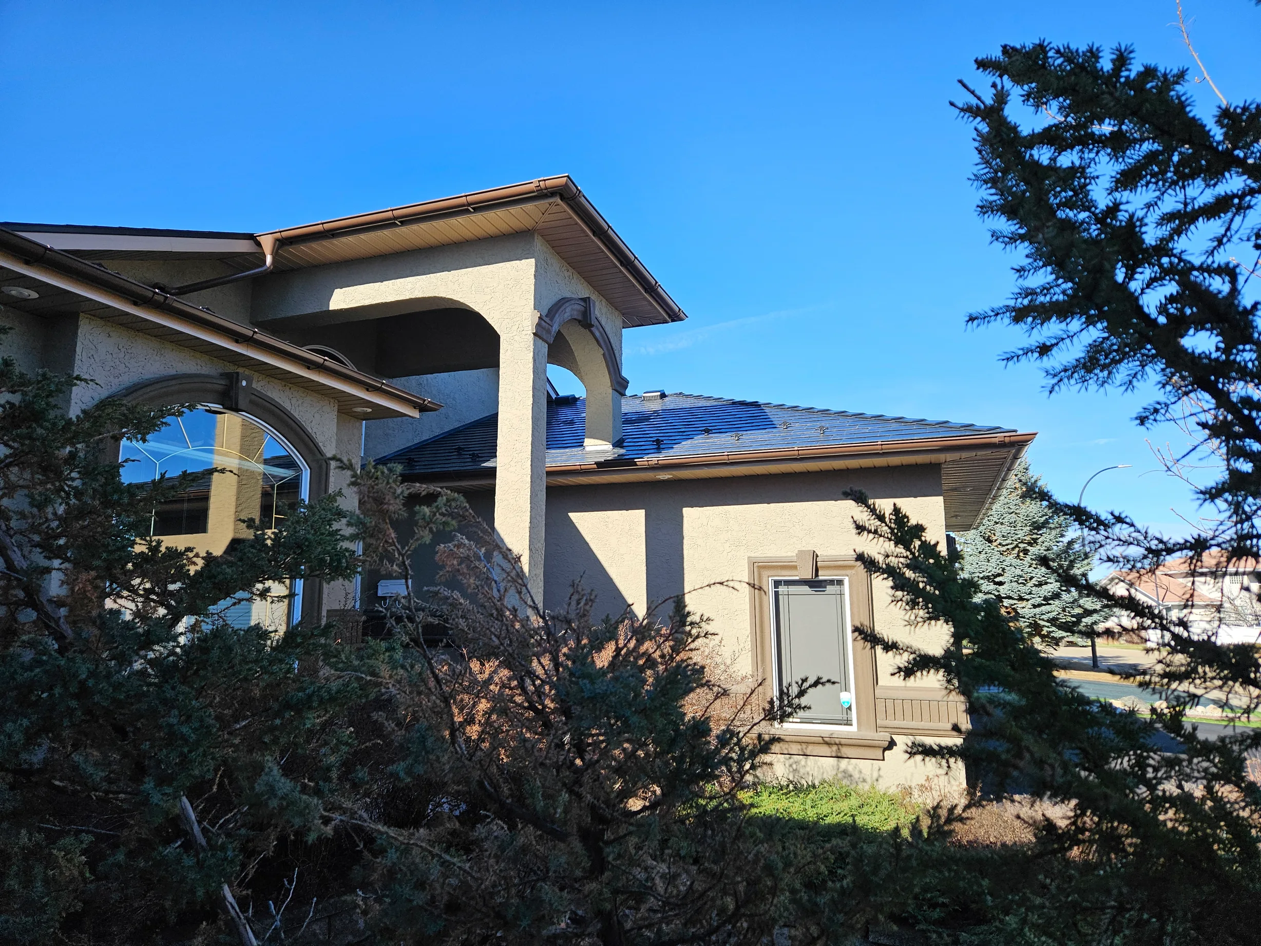 Black Interlock Slate aluminum roof on a single-storey home with a metal roof among trees, Red Deer, Alberta