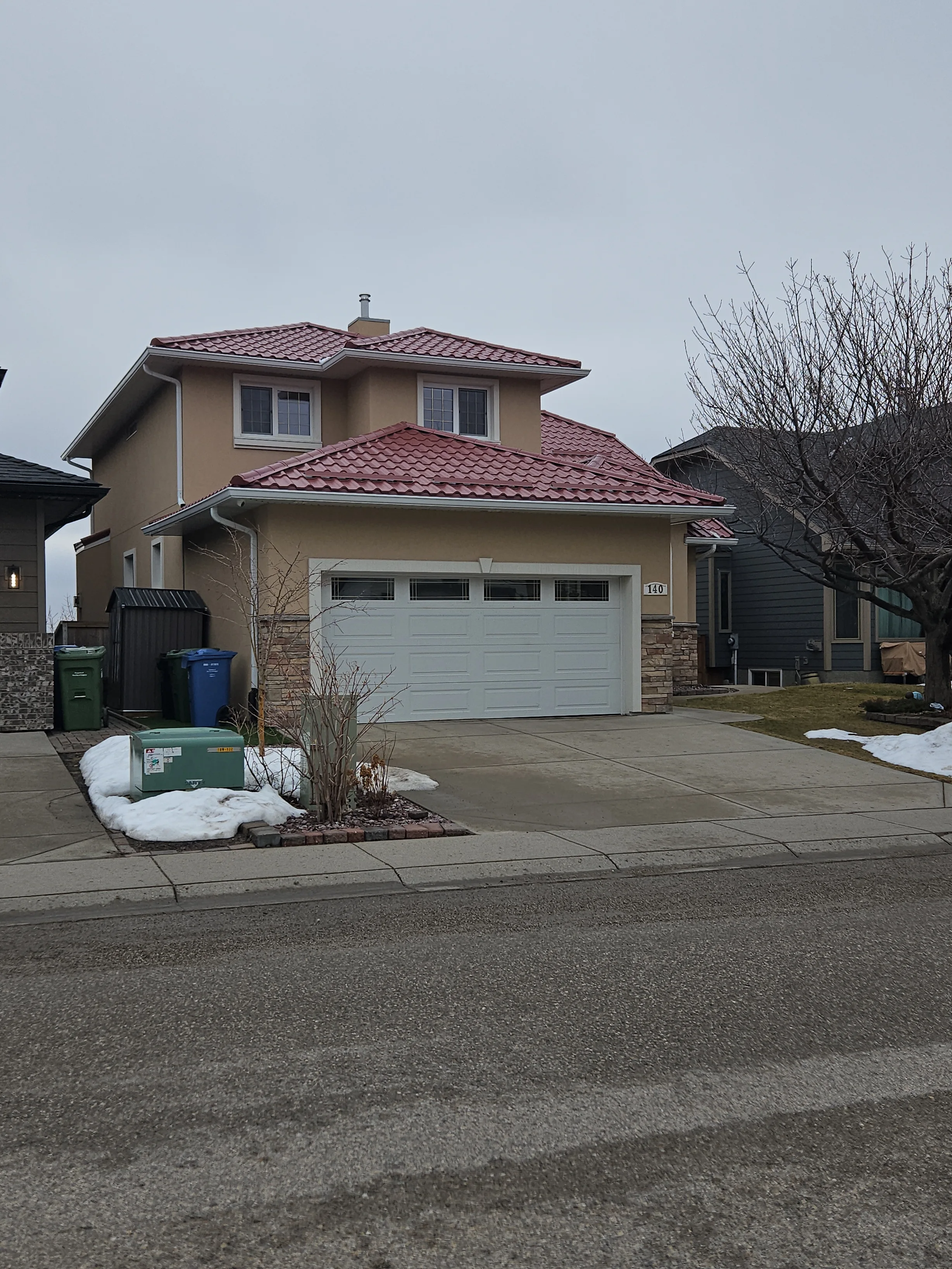 Tile Red Interlock Tile aluminum roof on a tan two-storey home with a red metal roof in an urban, Calgary, Alberta