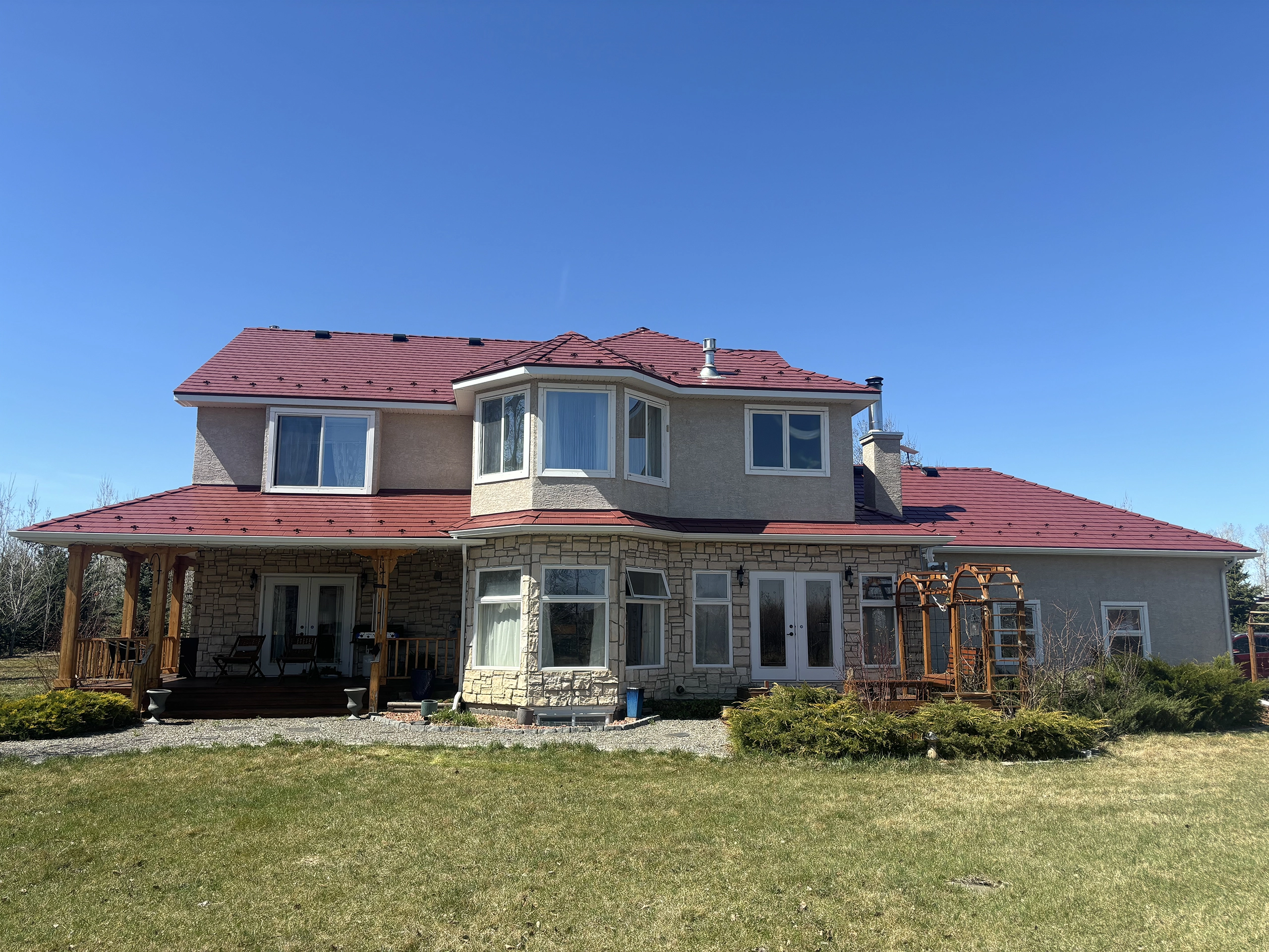 Rear elevation of a two-storey acreage home in Foothills County AB featuring Interlock Tile Red aluminum slate roofing with multi-hip complex rooflines.