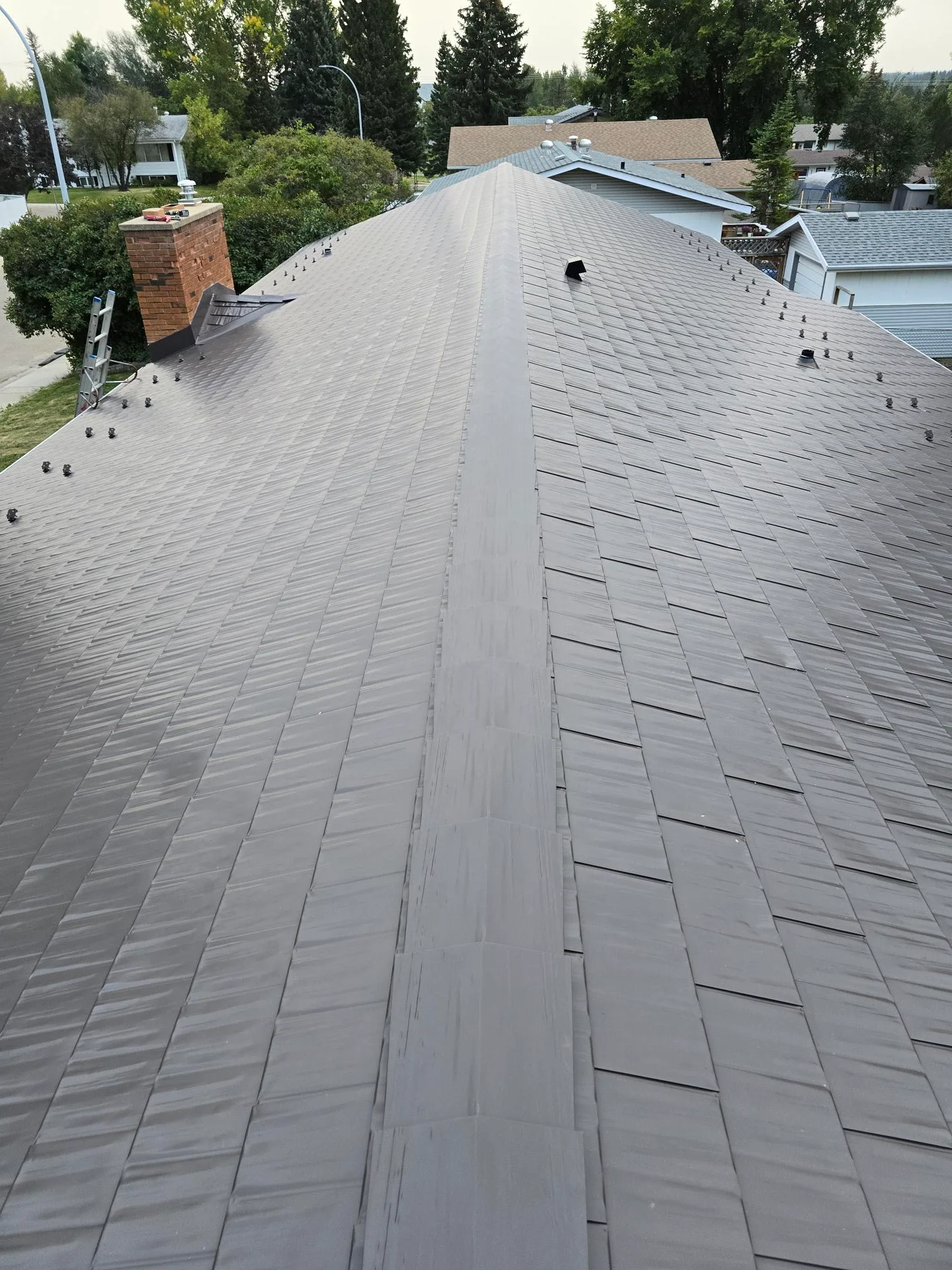 Tudor Brown Interlock Cedar Shingle aluminum roof on a Tudor-style home with a brown roof among tall green trees, Rocky Mountain House, Alberta