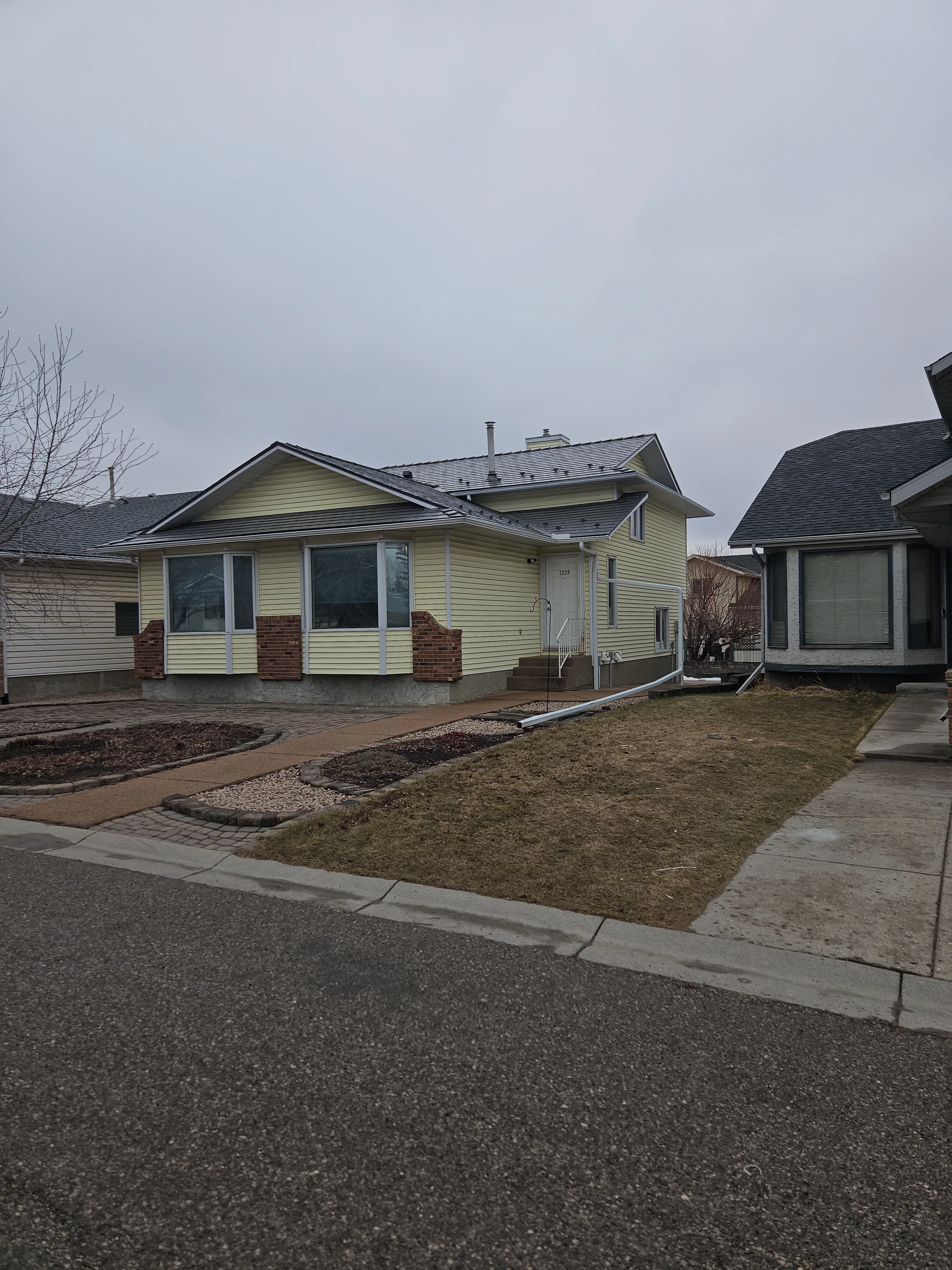 Musket Grey Interlock Slate aluminum roof on a yellow single-family home with a metal roof in a suburban, Calgary, Alberta