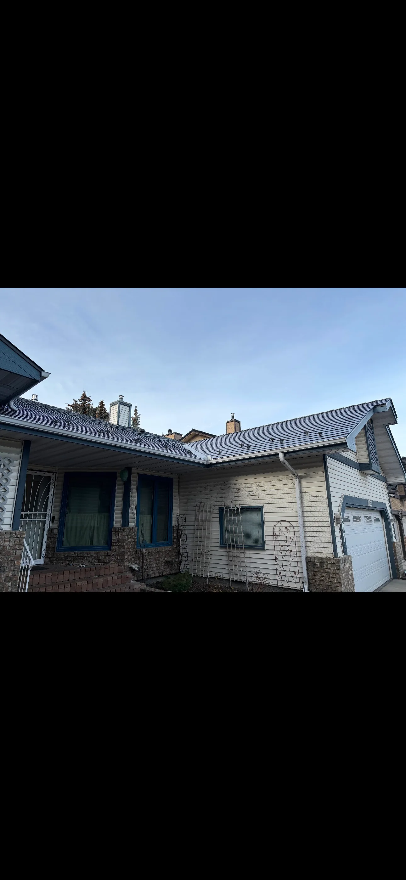 Musket Grey Interlock Slate aluminum roof on a beige single-family ranch home in the city under a blue, Calgary, Alberta