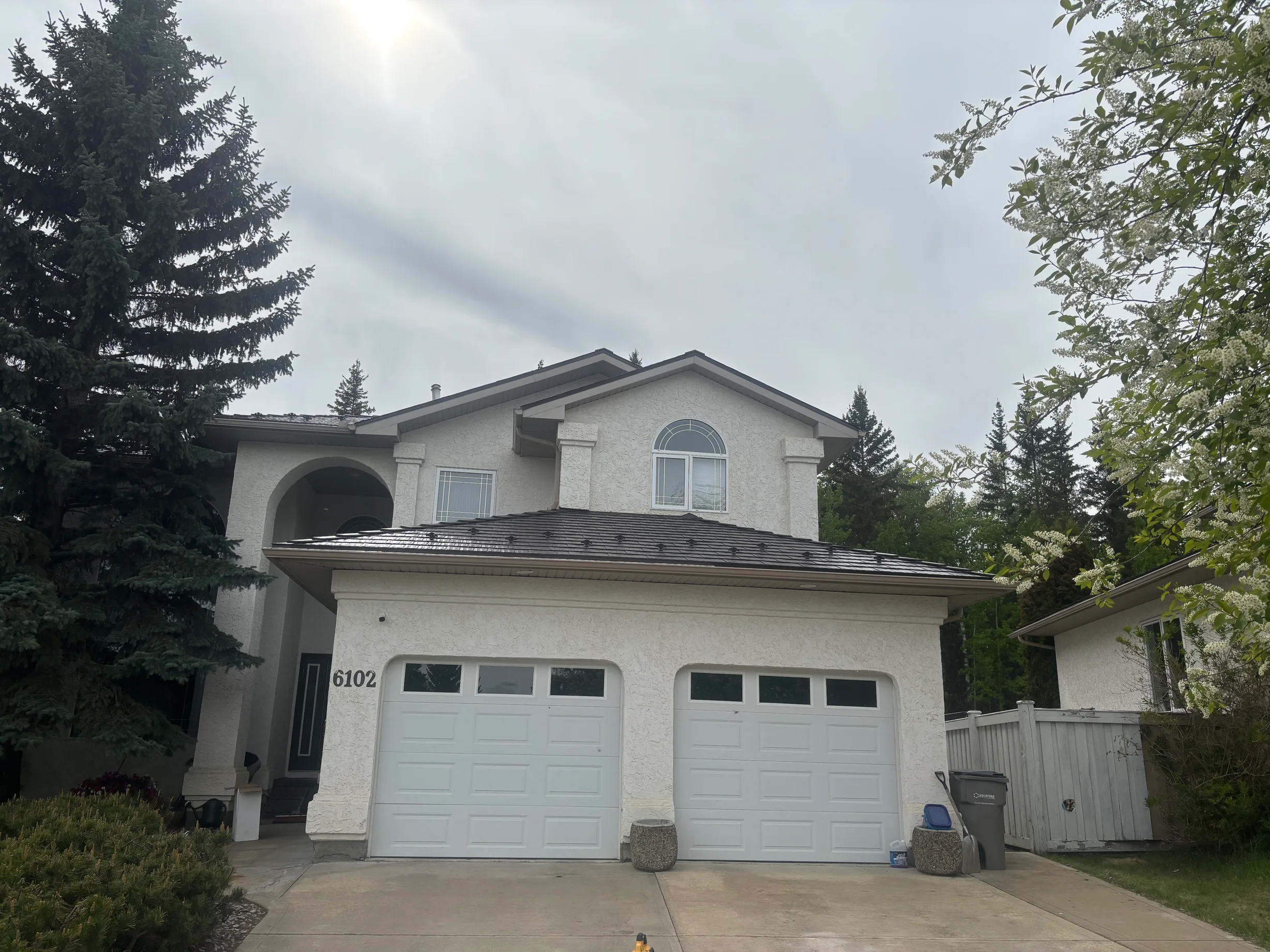 Tudor Brown Interlock Cedar Shingle aluminum roof on a white two-storey Tudor home among tall trees in a, Grande Prairie, Alberta
