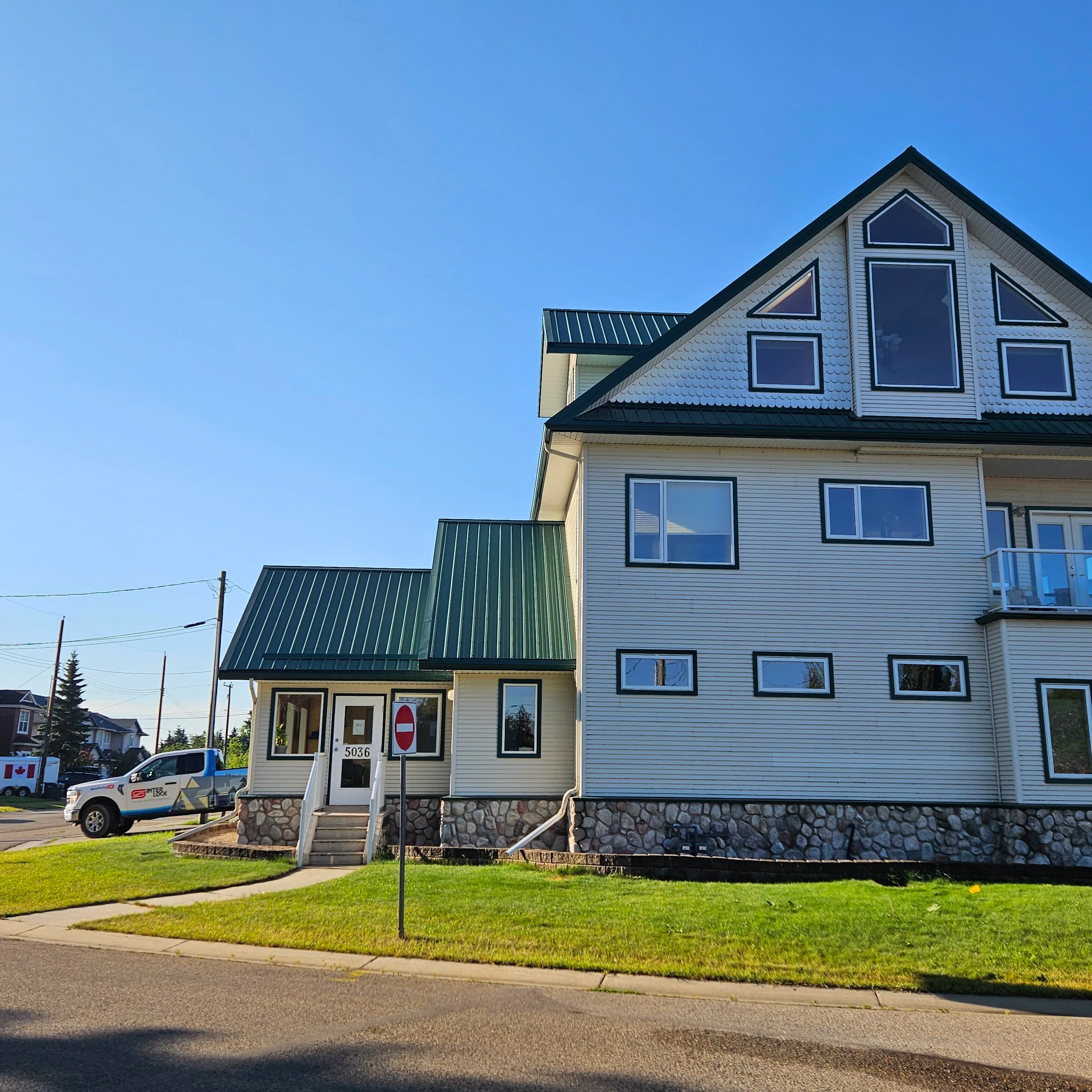 Hunter Green Interlock Cedar Shingle aluminum roof on a white two-storey cottage with dormers and a green metal, Sylvan Lake, Alberta