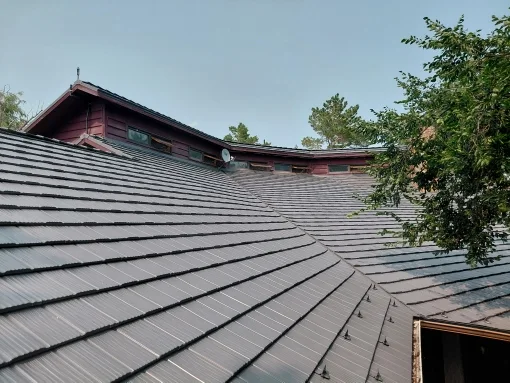 Musket Grey Interlock Shake aluminum roof on a red two-storey home with dormers among tall trees, Warner, Alberta