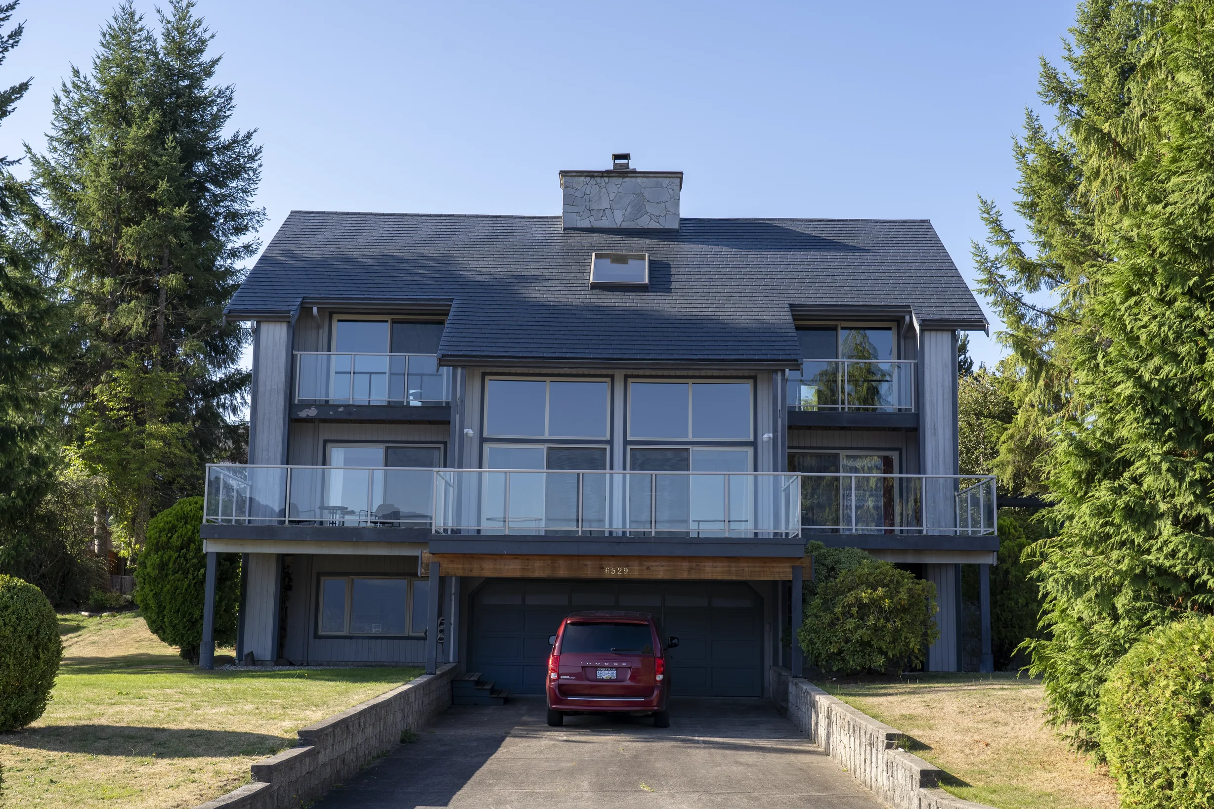 Deep Charcoal Interlock Slate aluminum roof on a two-storey home with a balcony and a red car in the garage, Sechelt, British Columbia