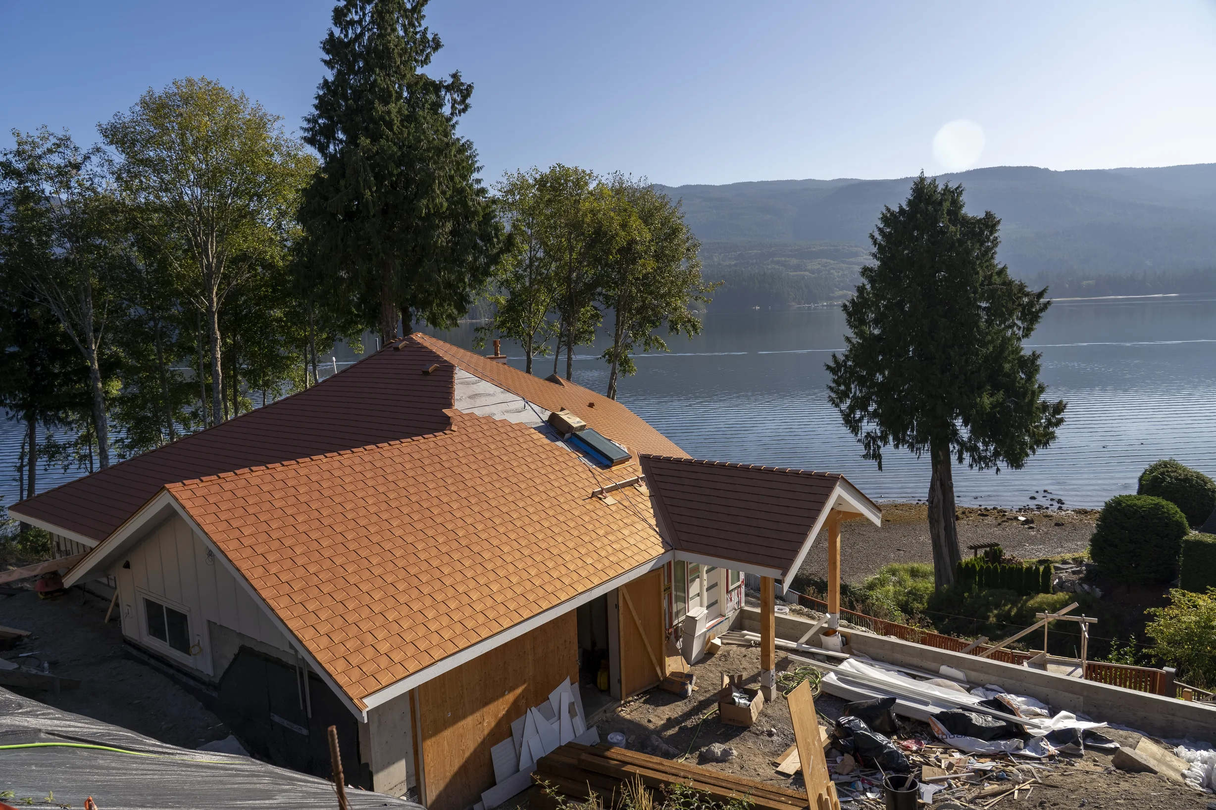 Copper Penny Interlock Slate aluminum roof being installed on a brown house with copper roof and dormers on a waterfront, Sechelt, British Columbia